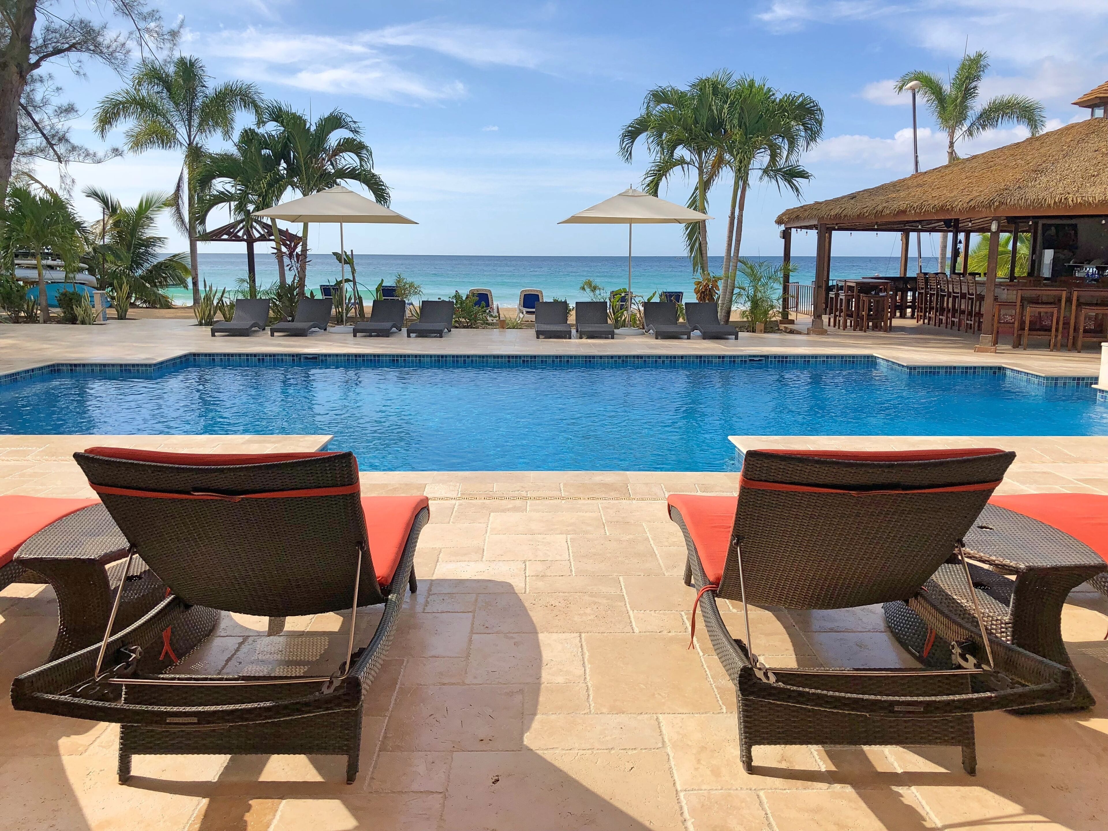Two lounge chairs between the pool and the sea.