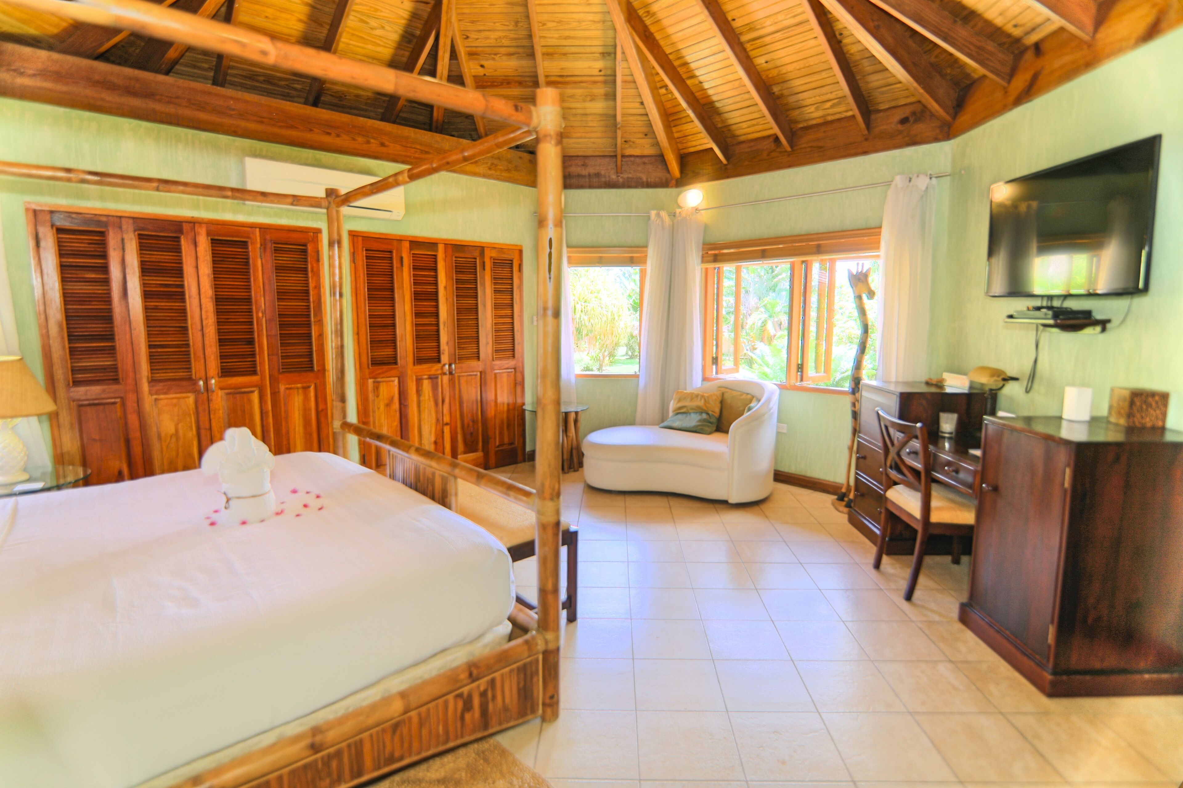 A bedroom with a bamboo four-poster bed and a lounge chair.