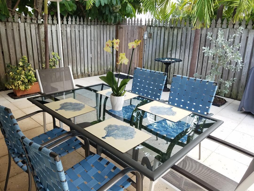 A glass dining table with six blue chairs on the patio.