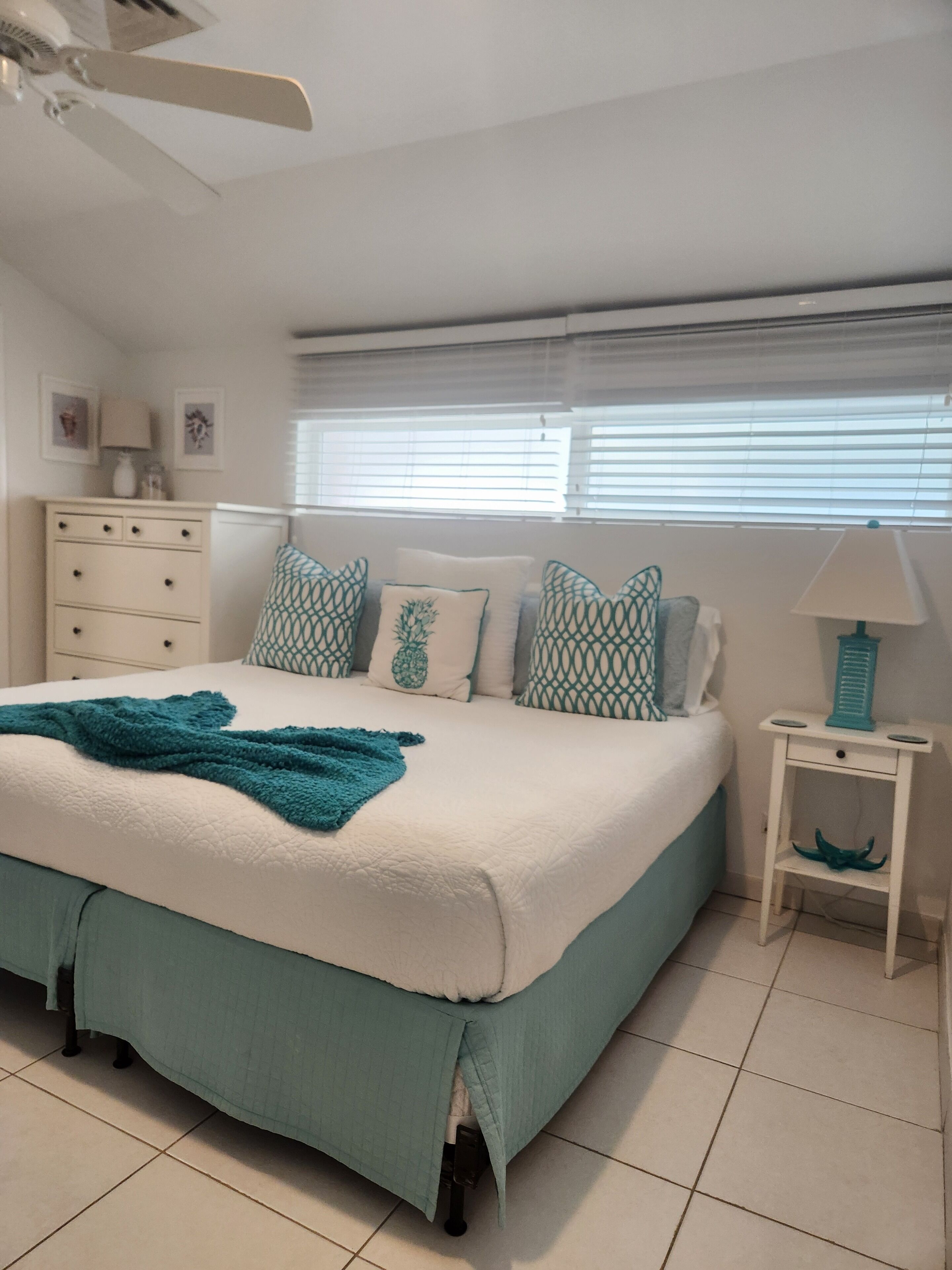 A bedroom with a bed, teal pillows, and a white dresser.