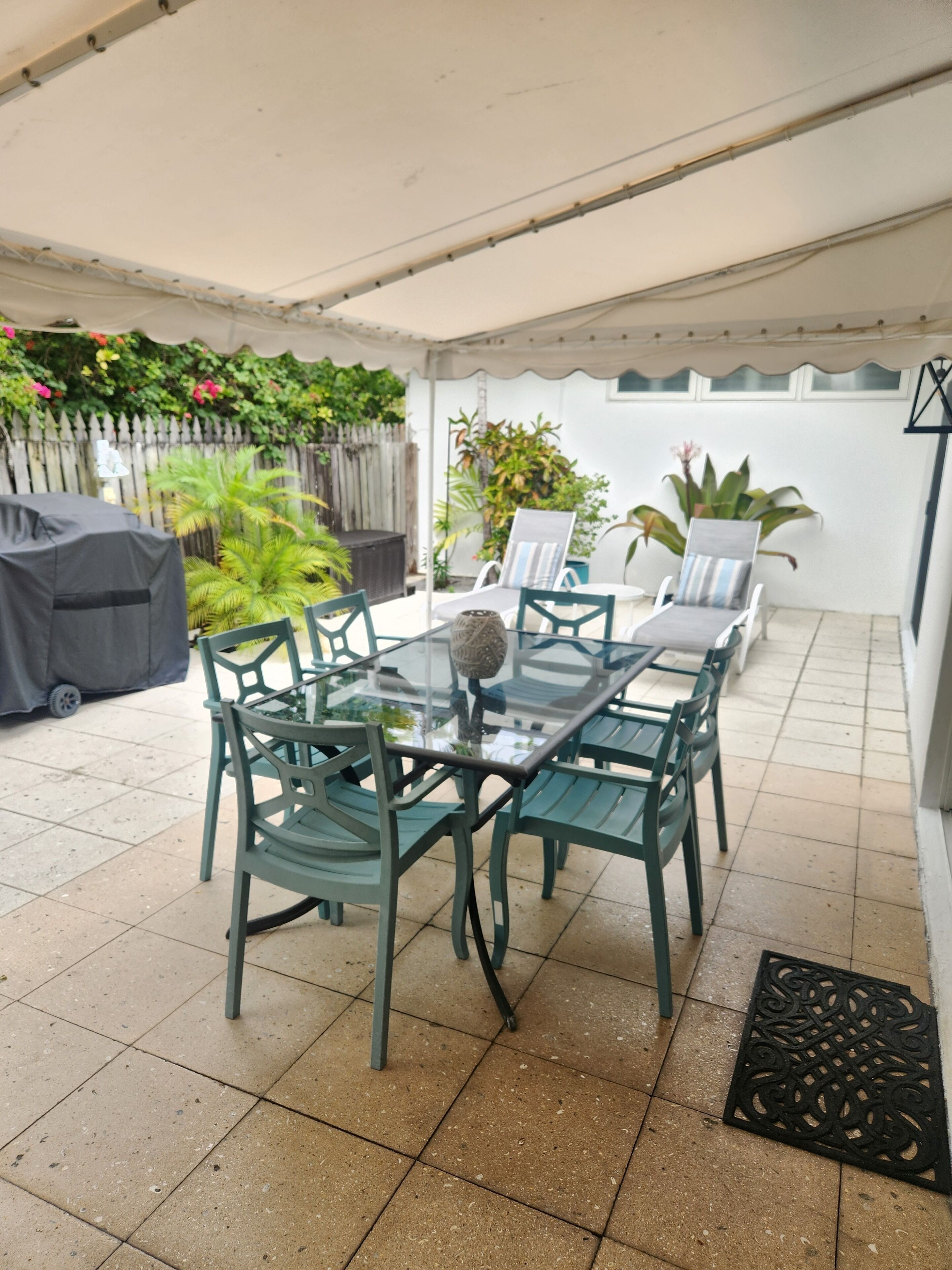 A covered patio with a dining table, sun loungers, and a grill.