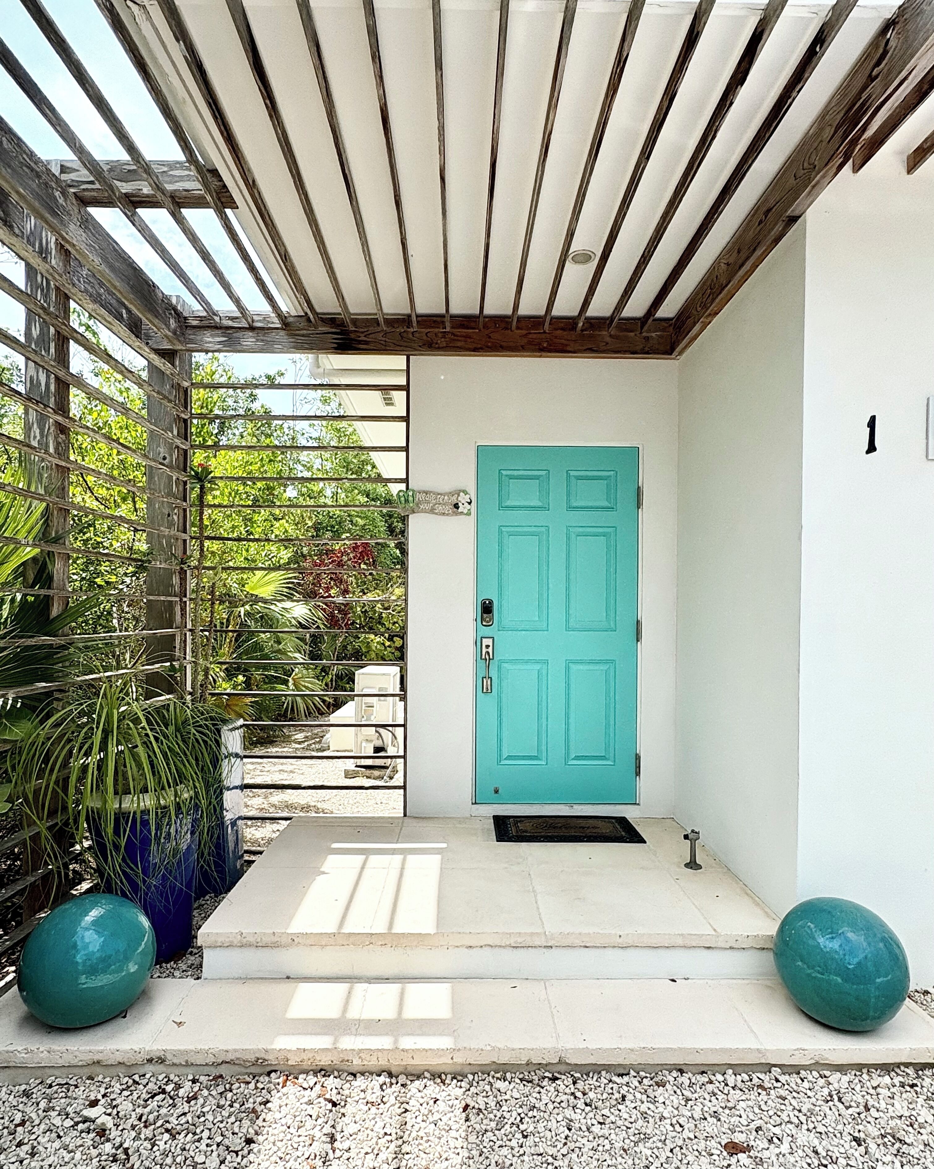 The entrance has a turquoise door under a wood pergola.