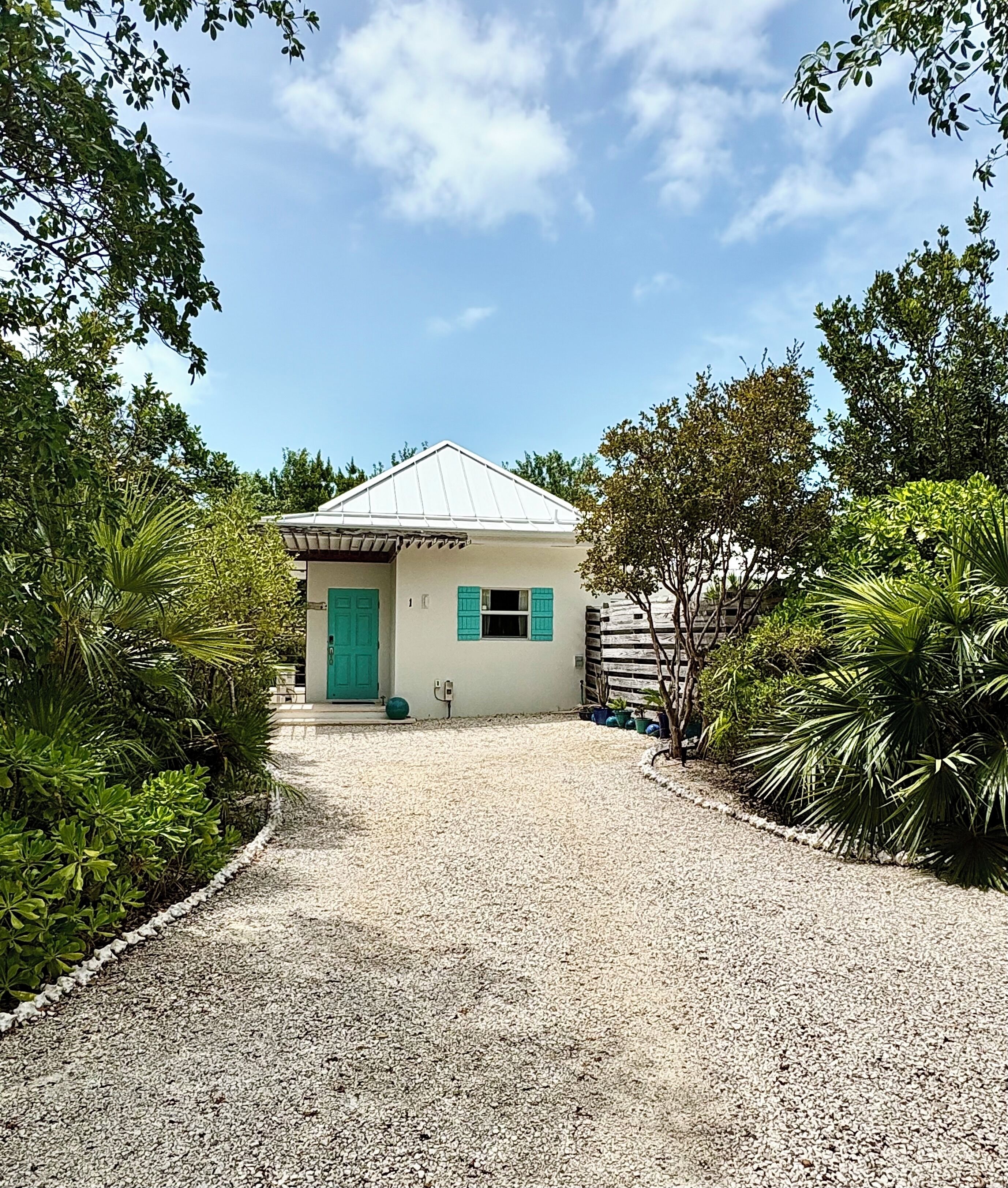 A gravel driveway leads to the villa between tropical plants.