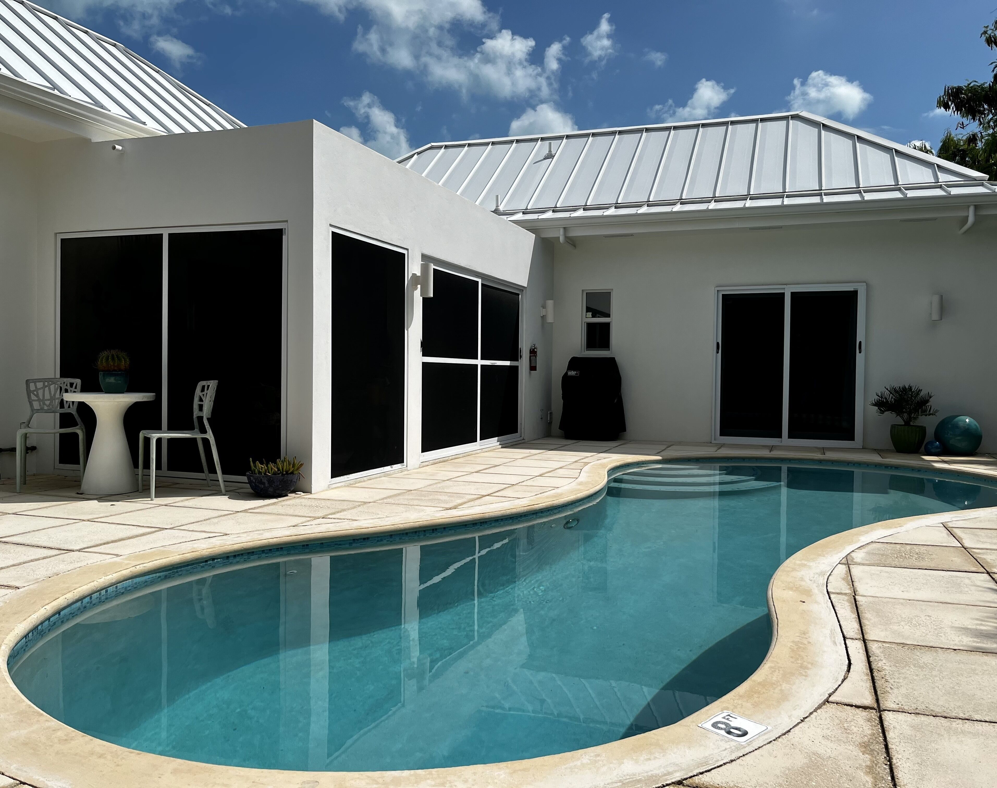 The pool deck has a small table and two white chairs.