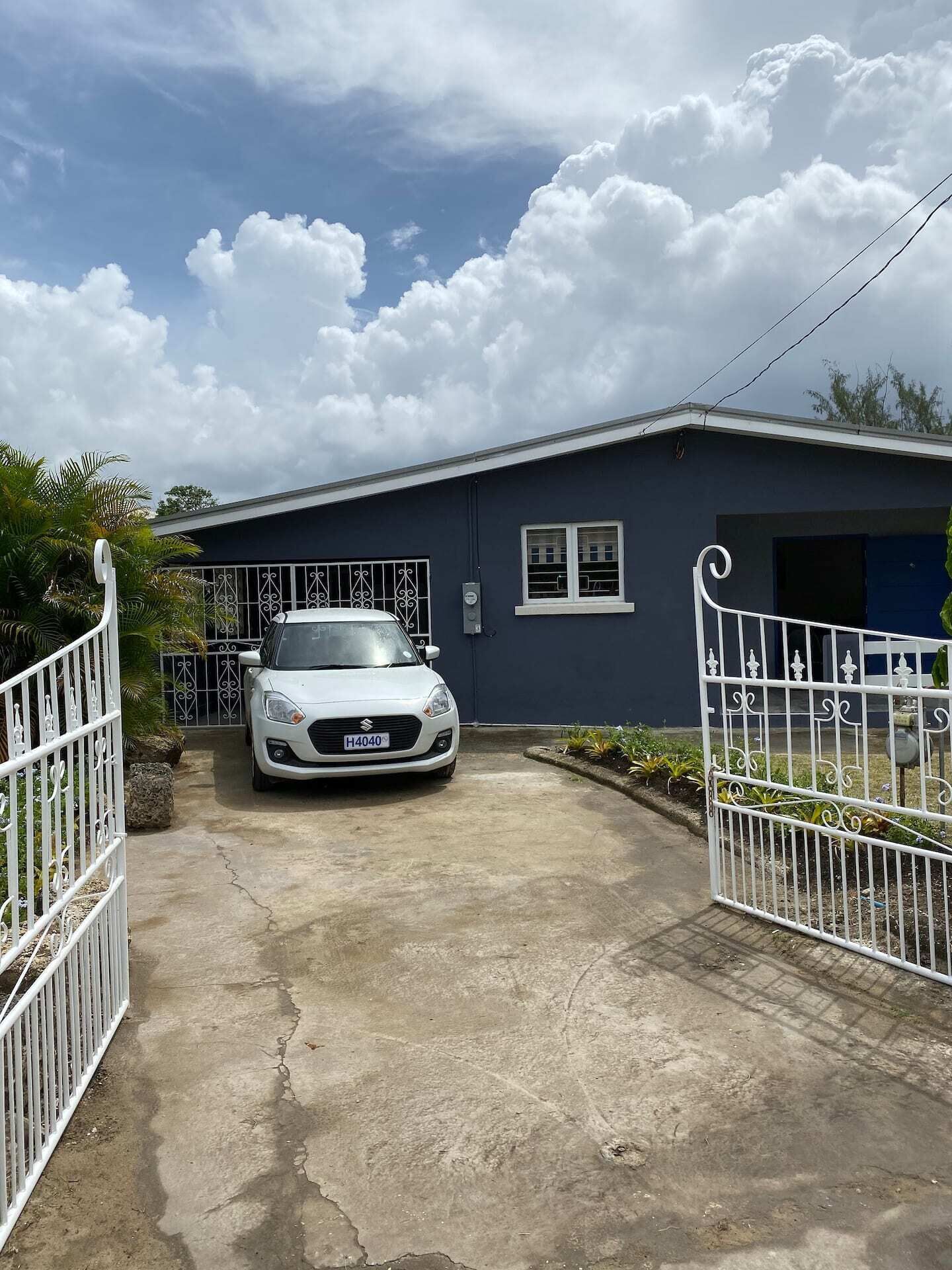 A view of the blue single-story house from the front gates.