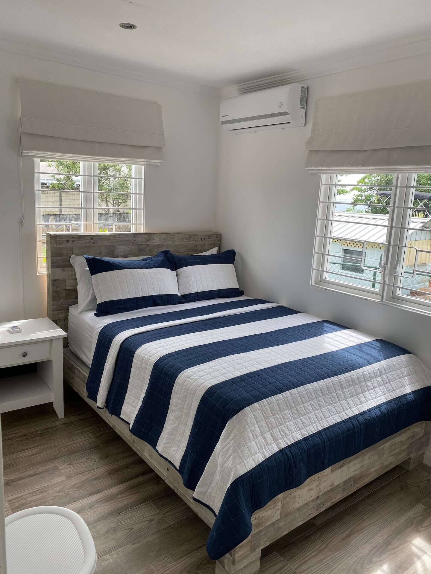 A bedroom with a double bed, two windows, and an air conditioner.