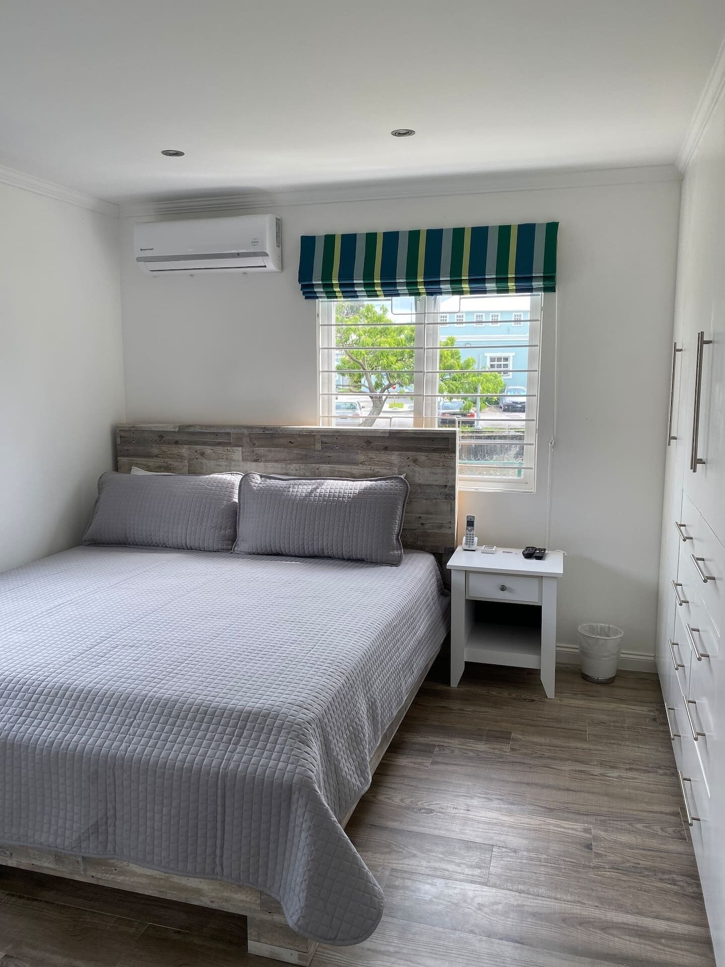 A bedroom with a double bed, a wardrobe, and a striped window blind.