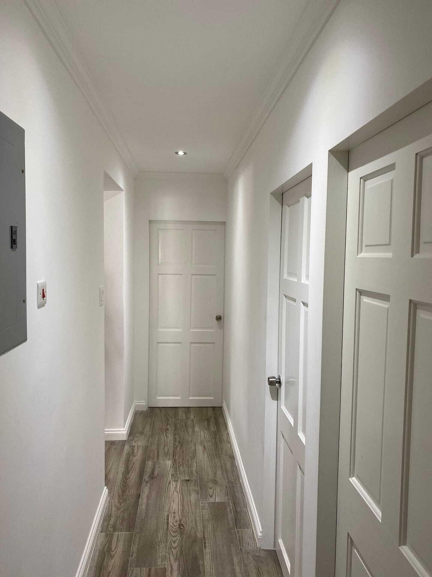 A hallway with white doors and a wood-look floor.