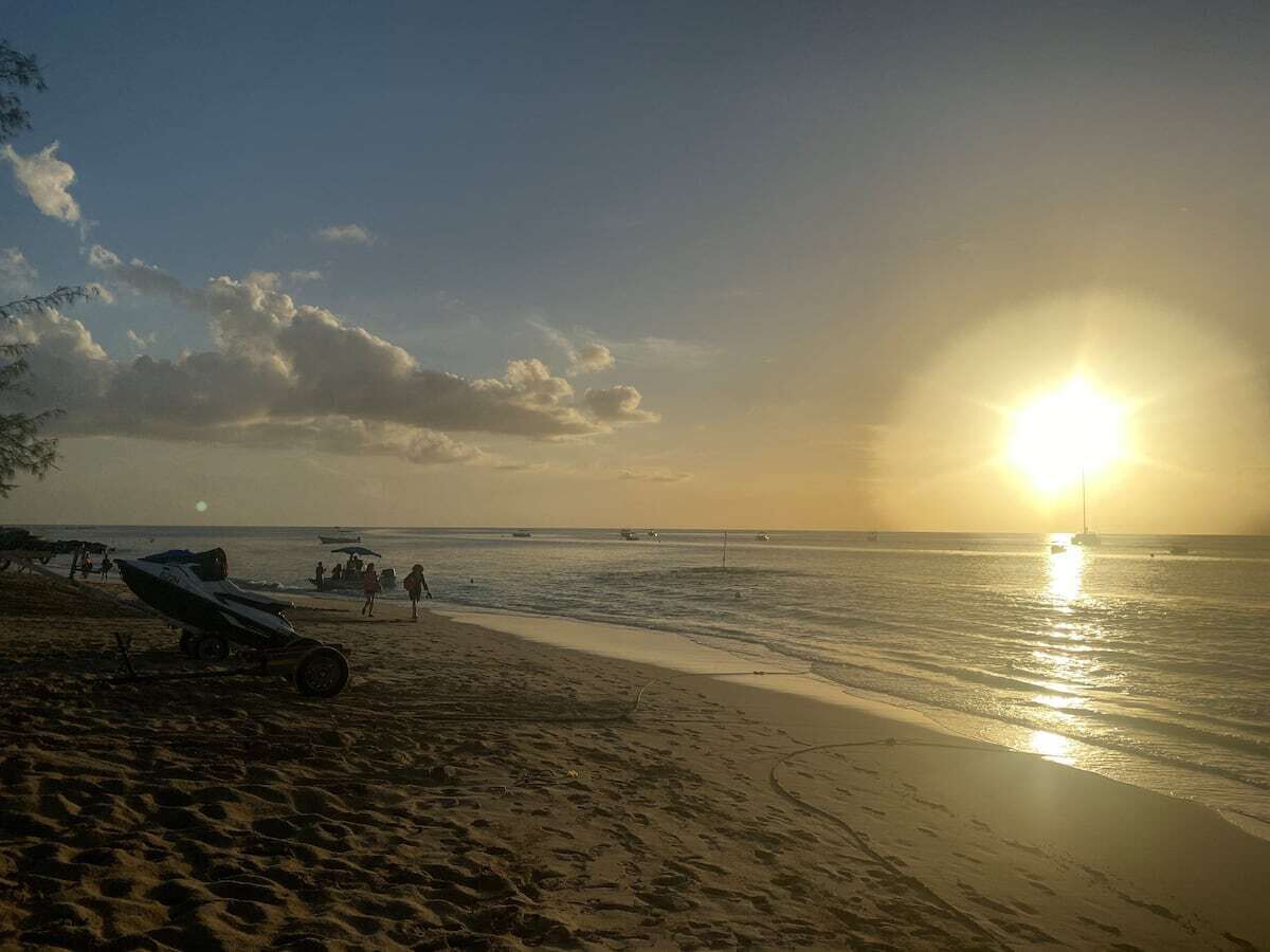 A beach at sunset with boats near the shore.