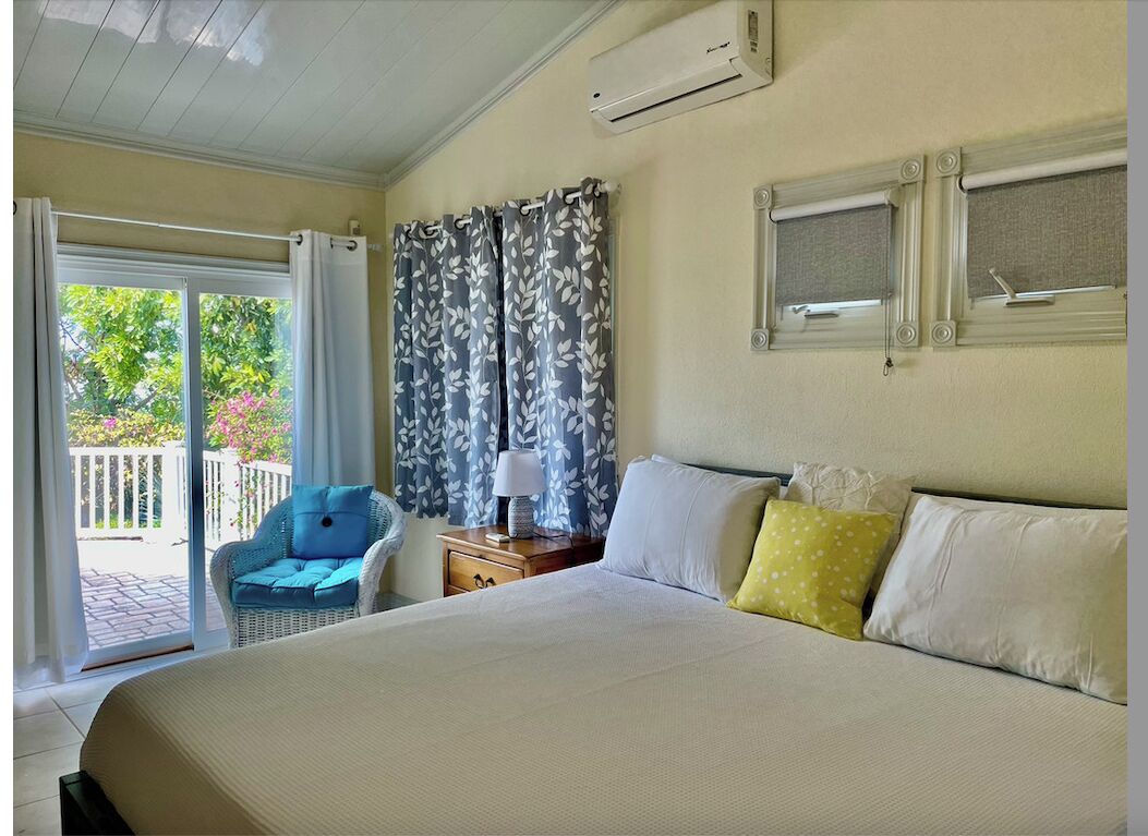 A bedroom with a bed, a wicker chair, and a glass door to the terrace.