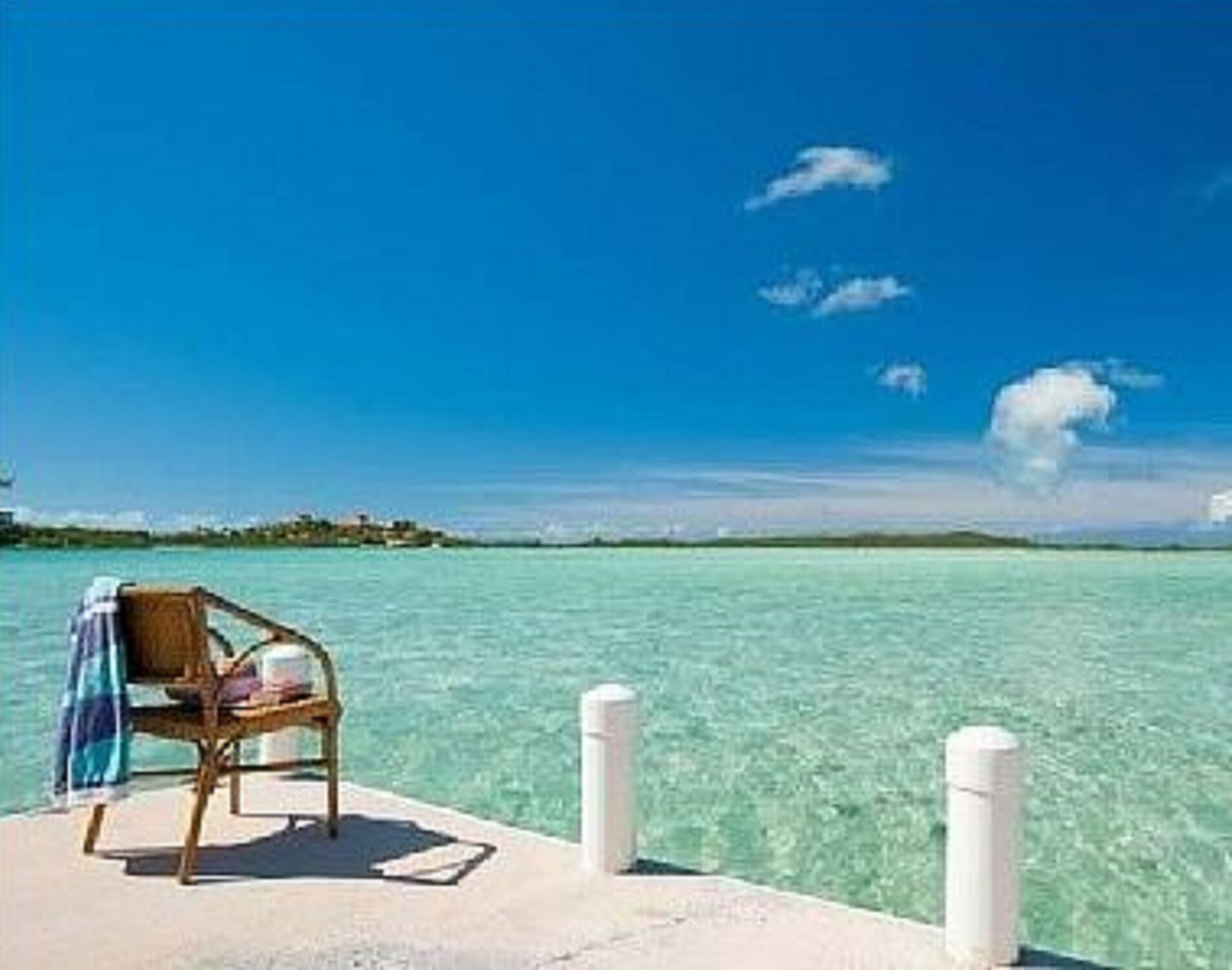 A chair with a towel on the dock next to shallow clear water.