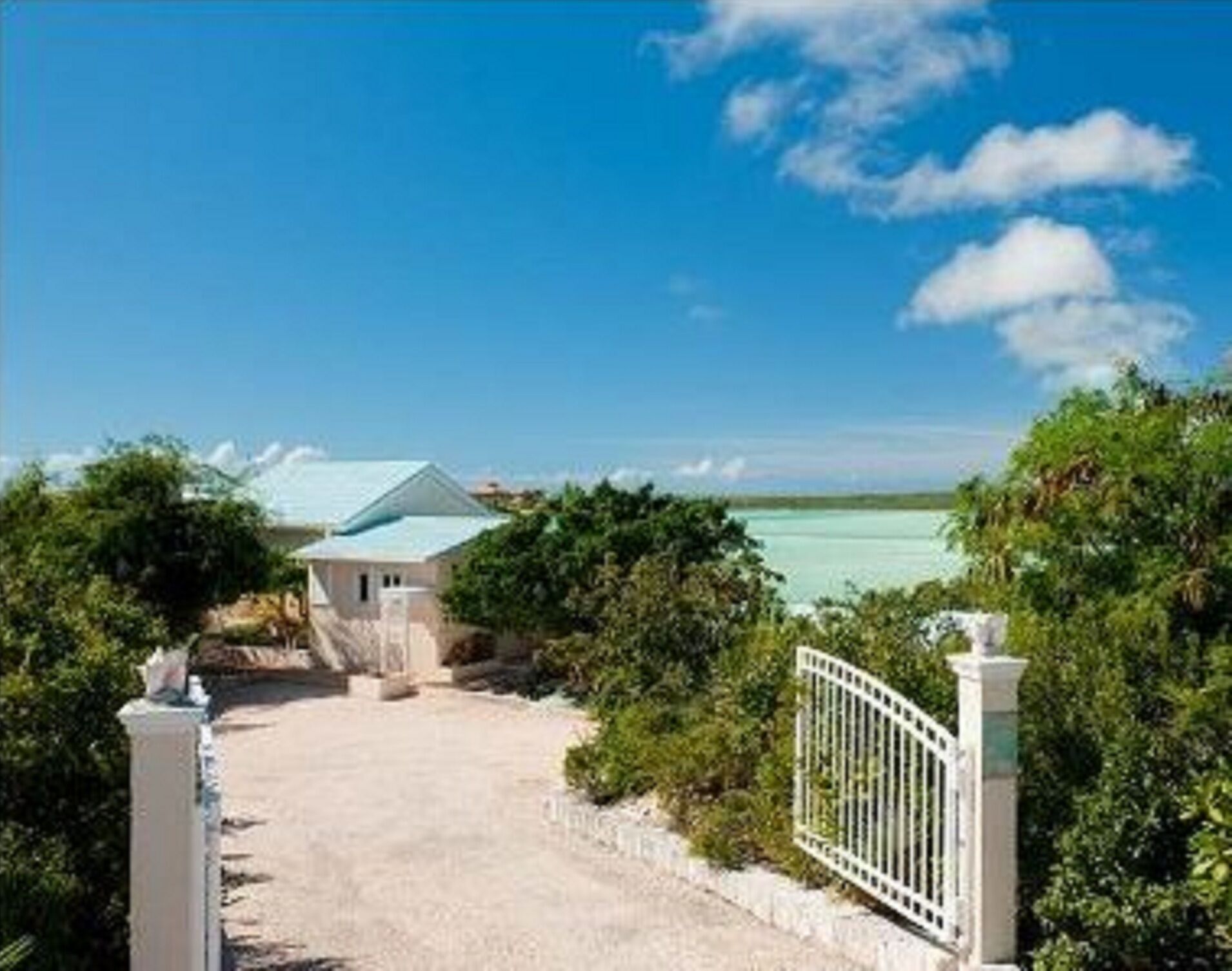 A gate and a gravel driveway with the villa and the water behind.