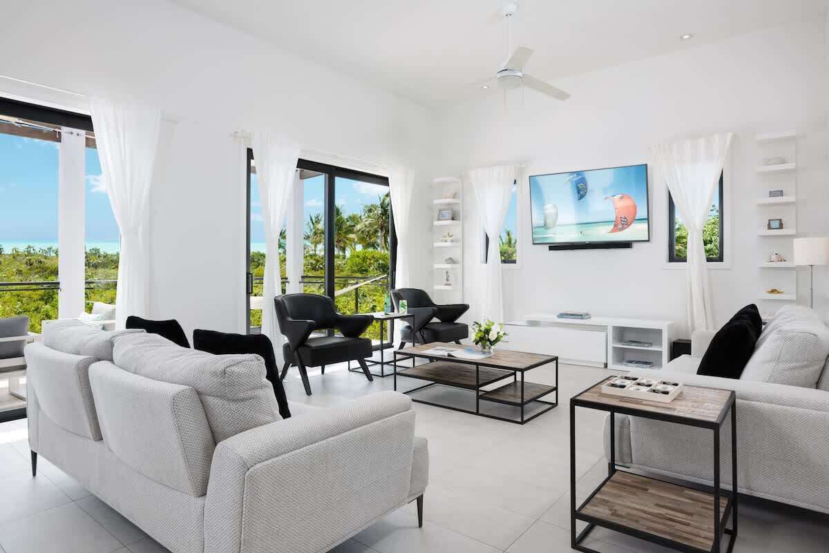 The living room has two sofas, a wall television, and windows with a view of the sea.