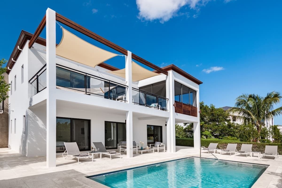 The two-story white villa stands behind the pool and a row of sun loungers.