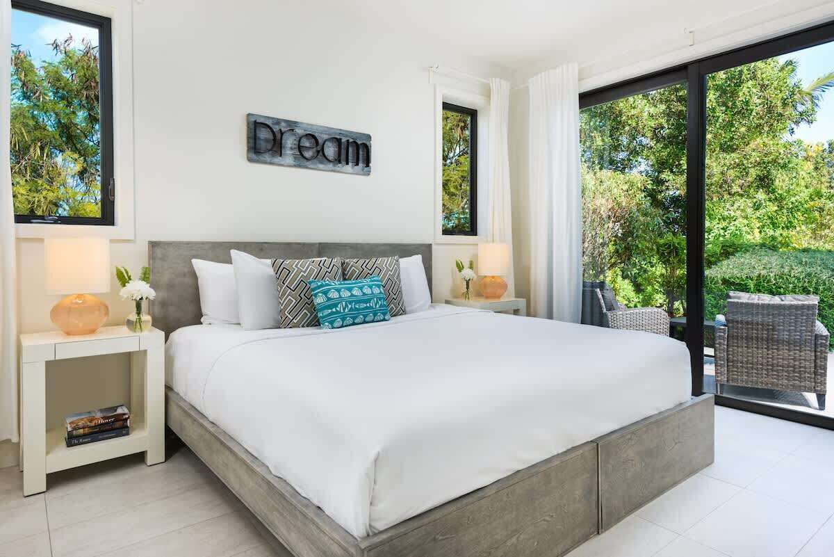 The bedroom has a large bed and glass doors to a terrace with two rattan chairs.
