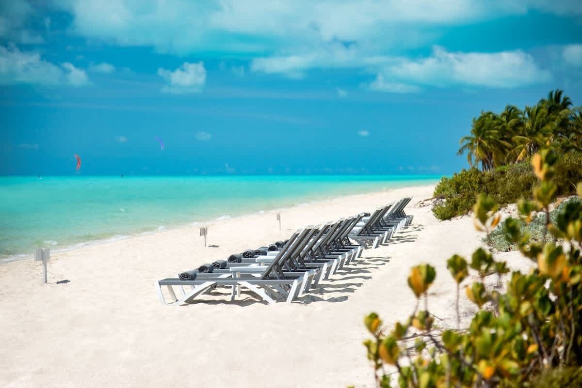 Rows of sun loungers stand on the white sand of Long Bay Beach.