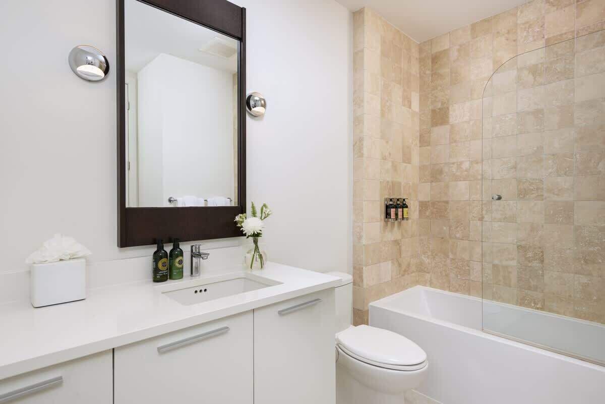 The bathroom has a vanity, a toilet, and a bathtub with a glass screen.