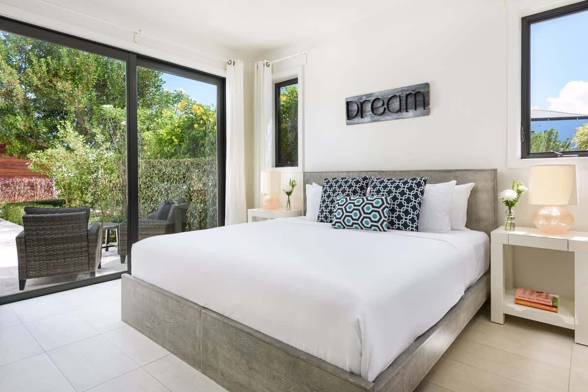 The bedroom has a large bed, two bedside tables with lamps, and a glass door to the garden.