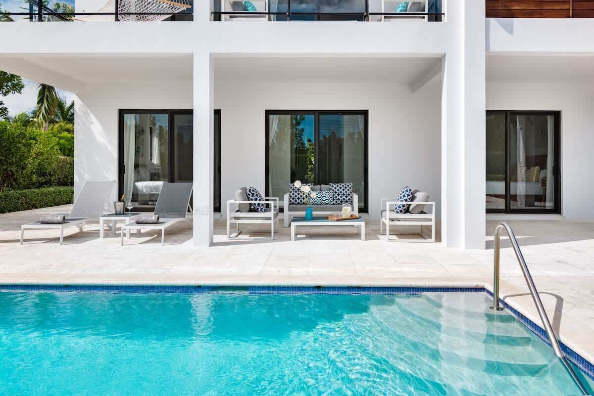 The pool lies in front of a covered terrace with outdoor seats and sun loungers.