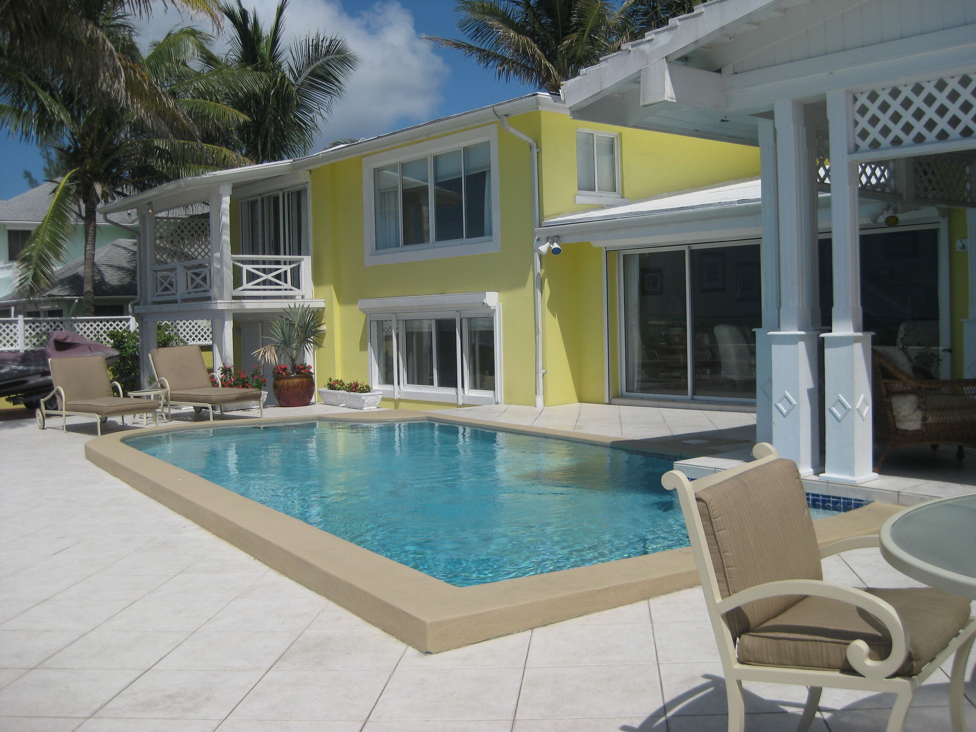 The pool and the terrace in front of the yellow two-story house.