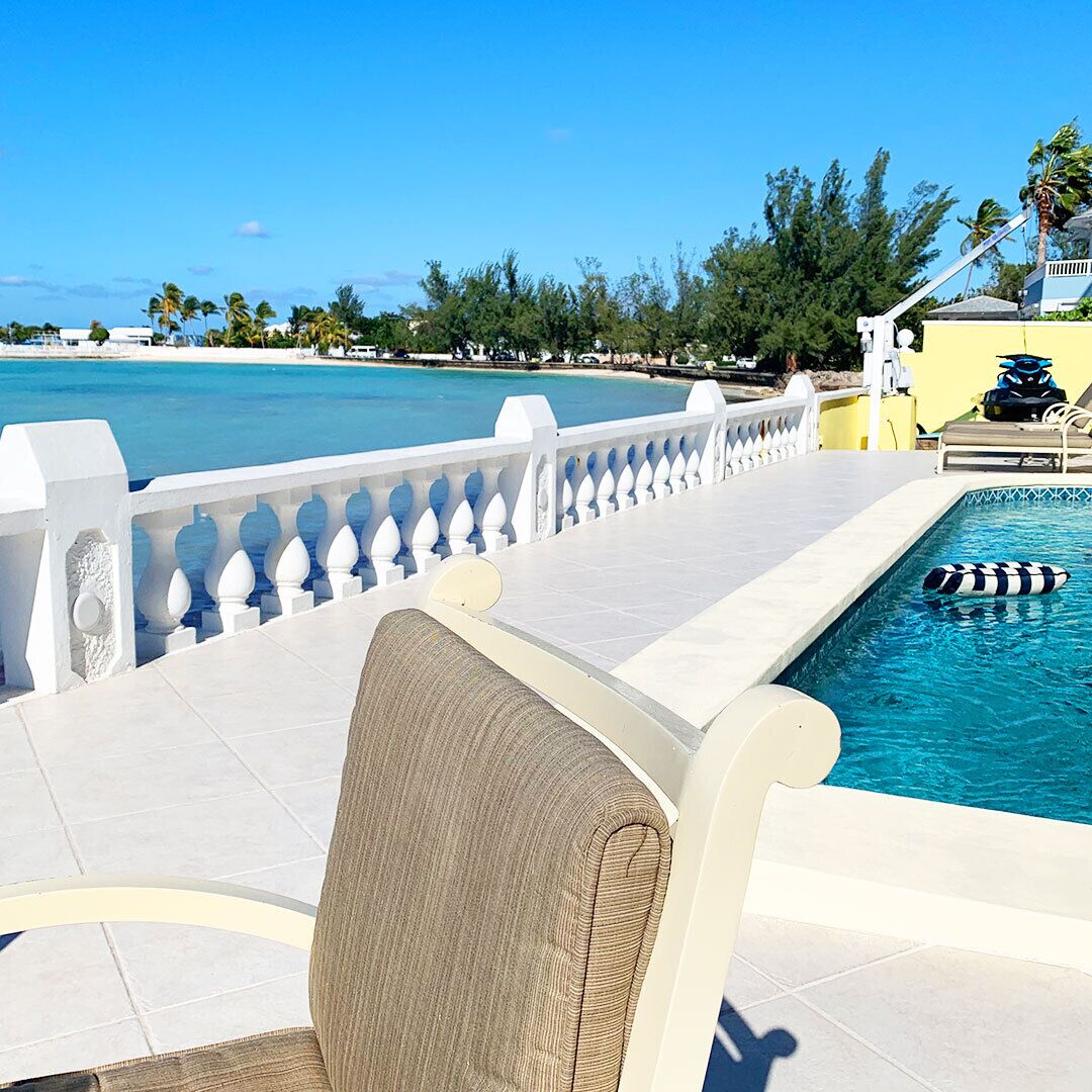 A cushioned chair next to the pool, with the sea beyond the white balustrade.