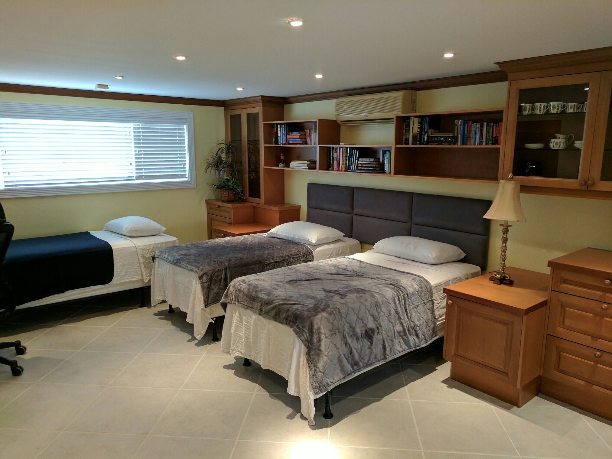 A room with three single beds, bookshelves, and a desk chair.