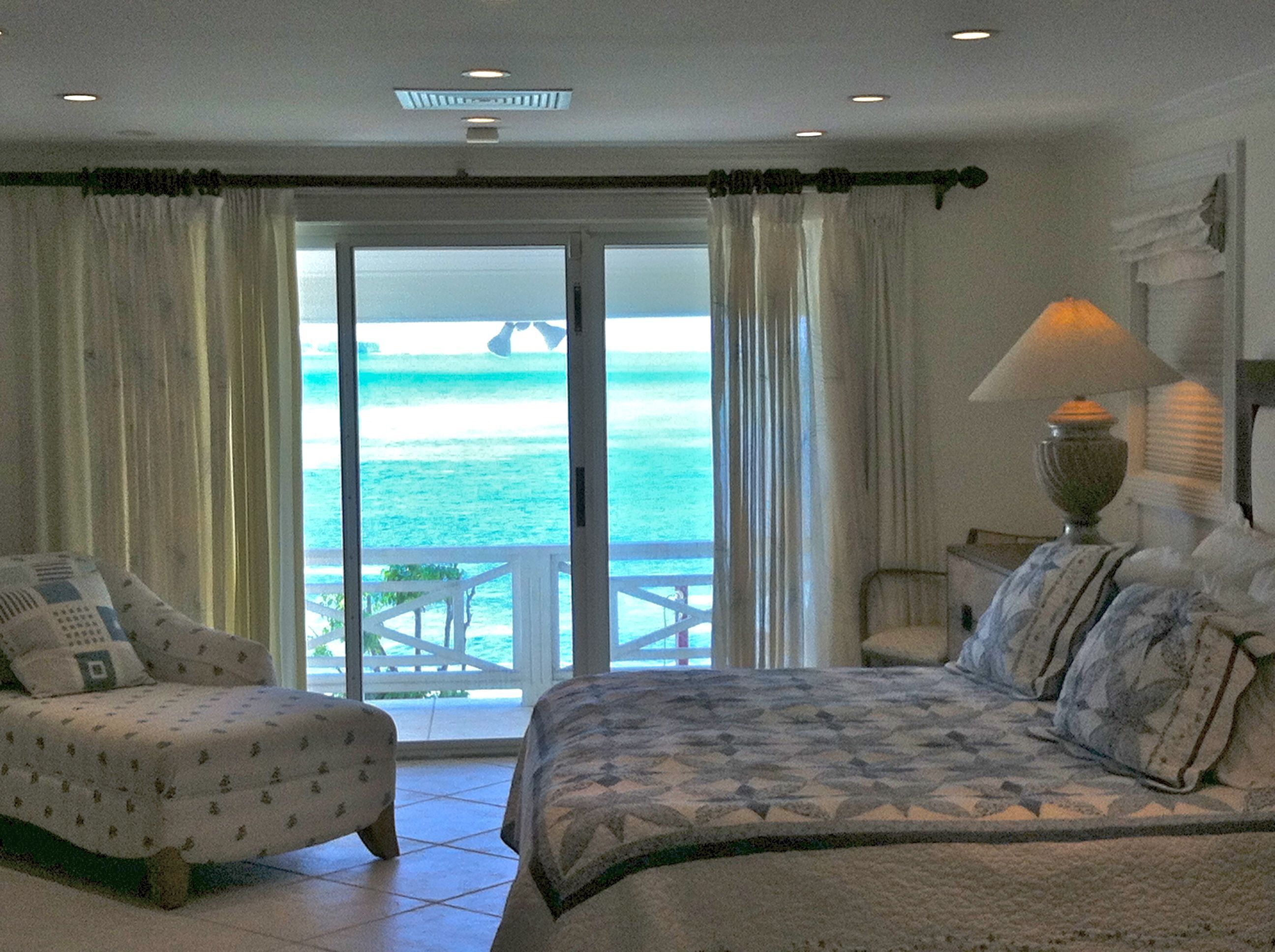 A bedroom with a sliding glass door that opens to a balcony above the sea.