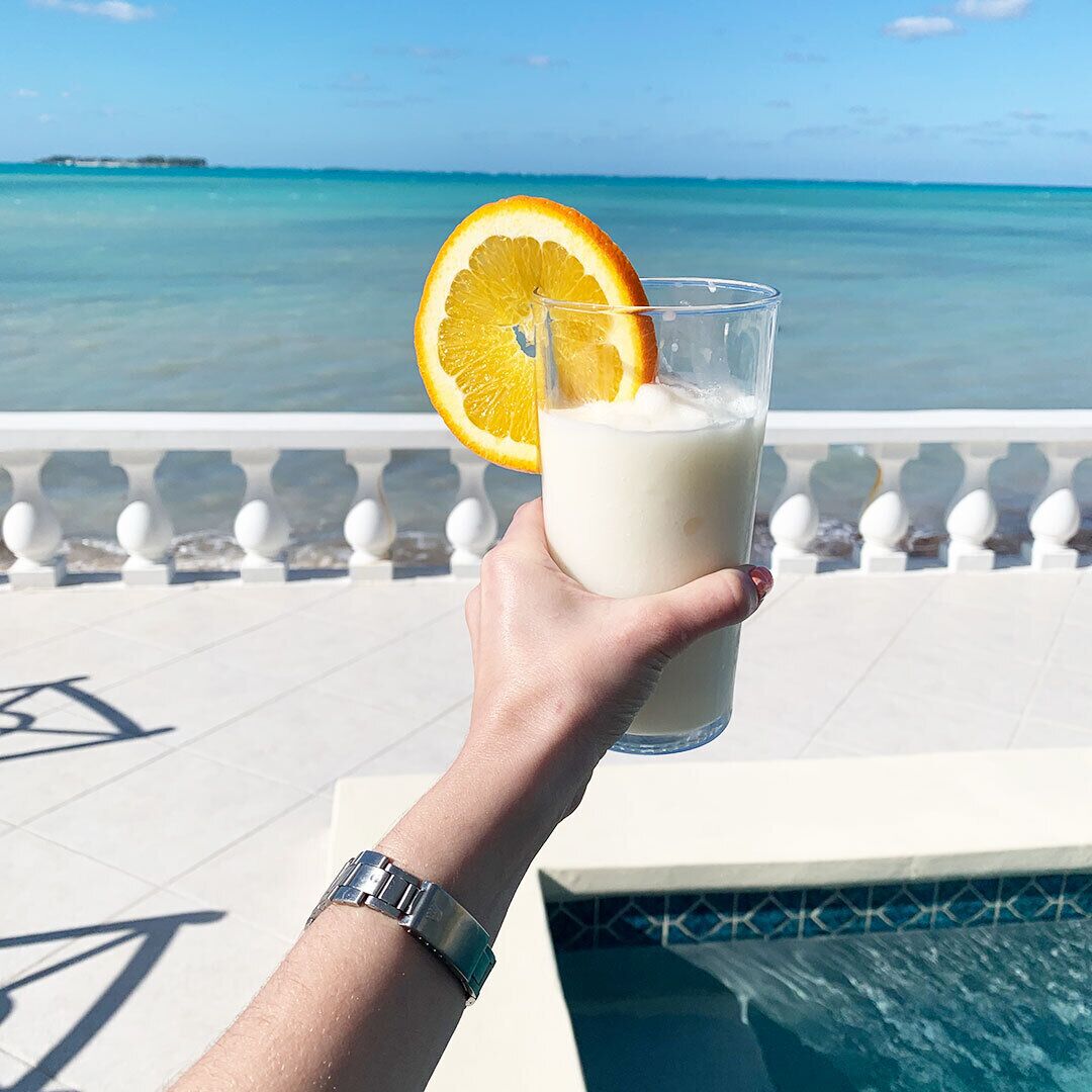 A hand holds a drink with an orange slice next to the pool.