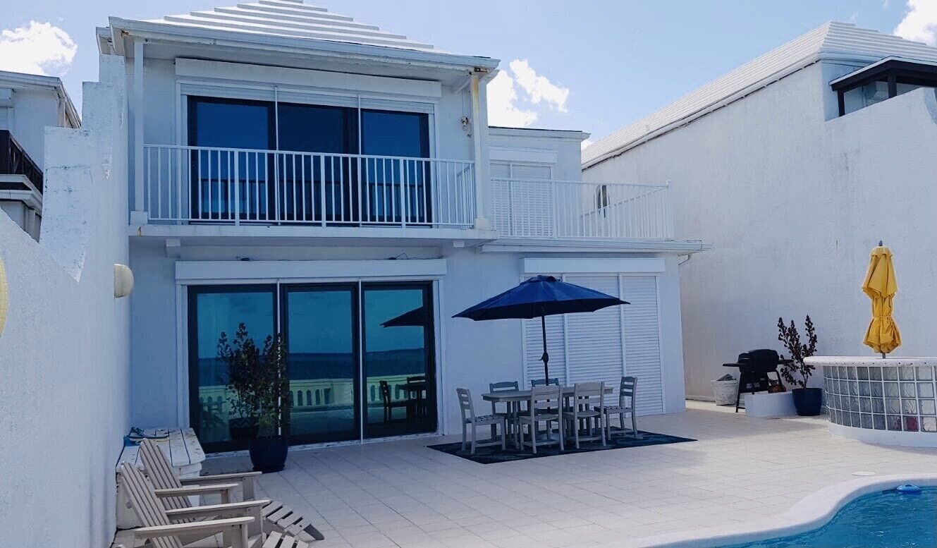 The white two-story villa with a patio, a dining table, and the pool.