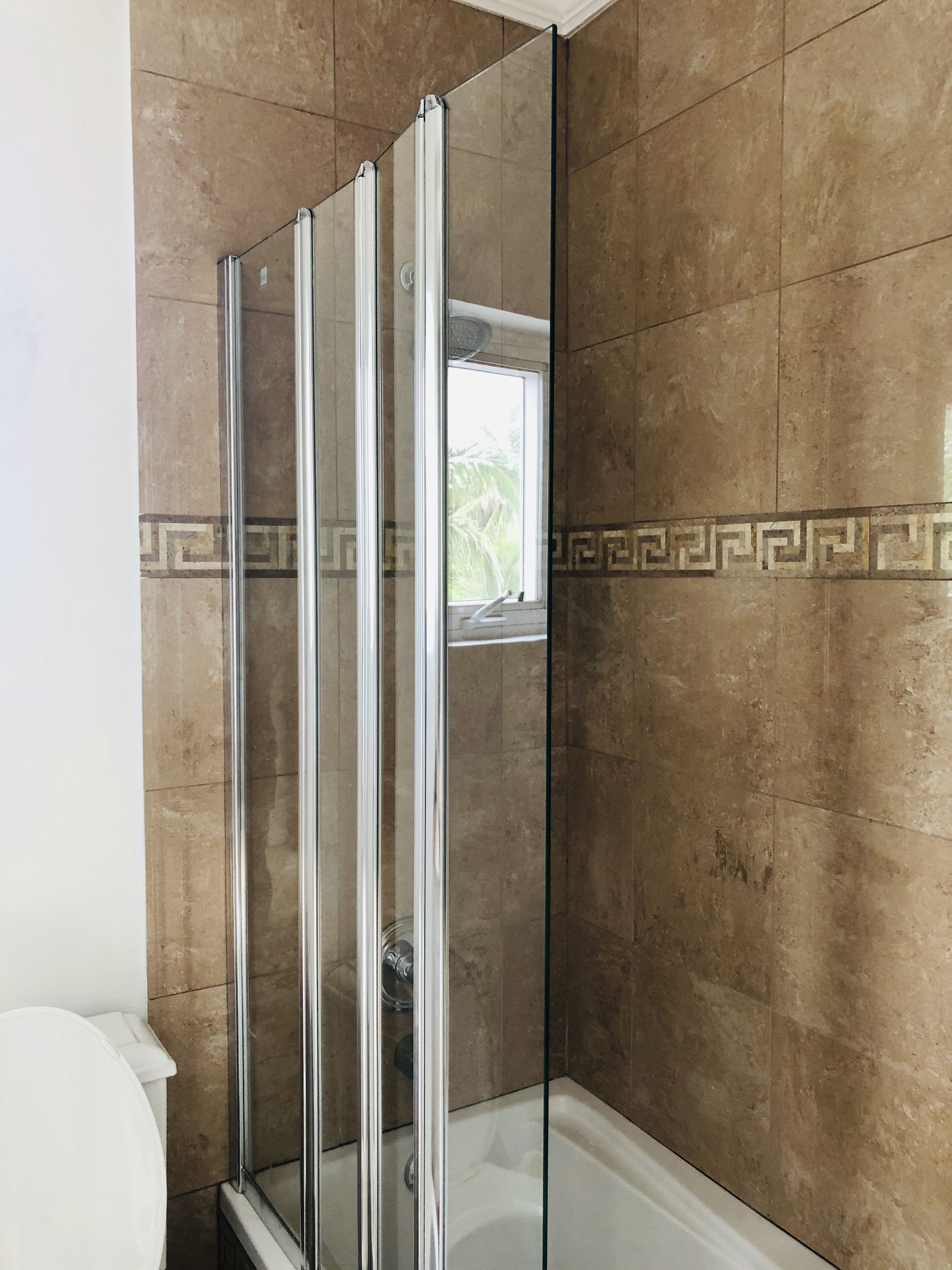 A bathroom with folding glass shower doors and brown tile.