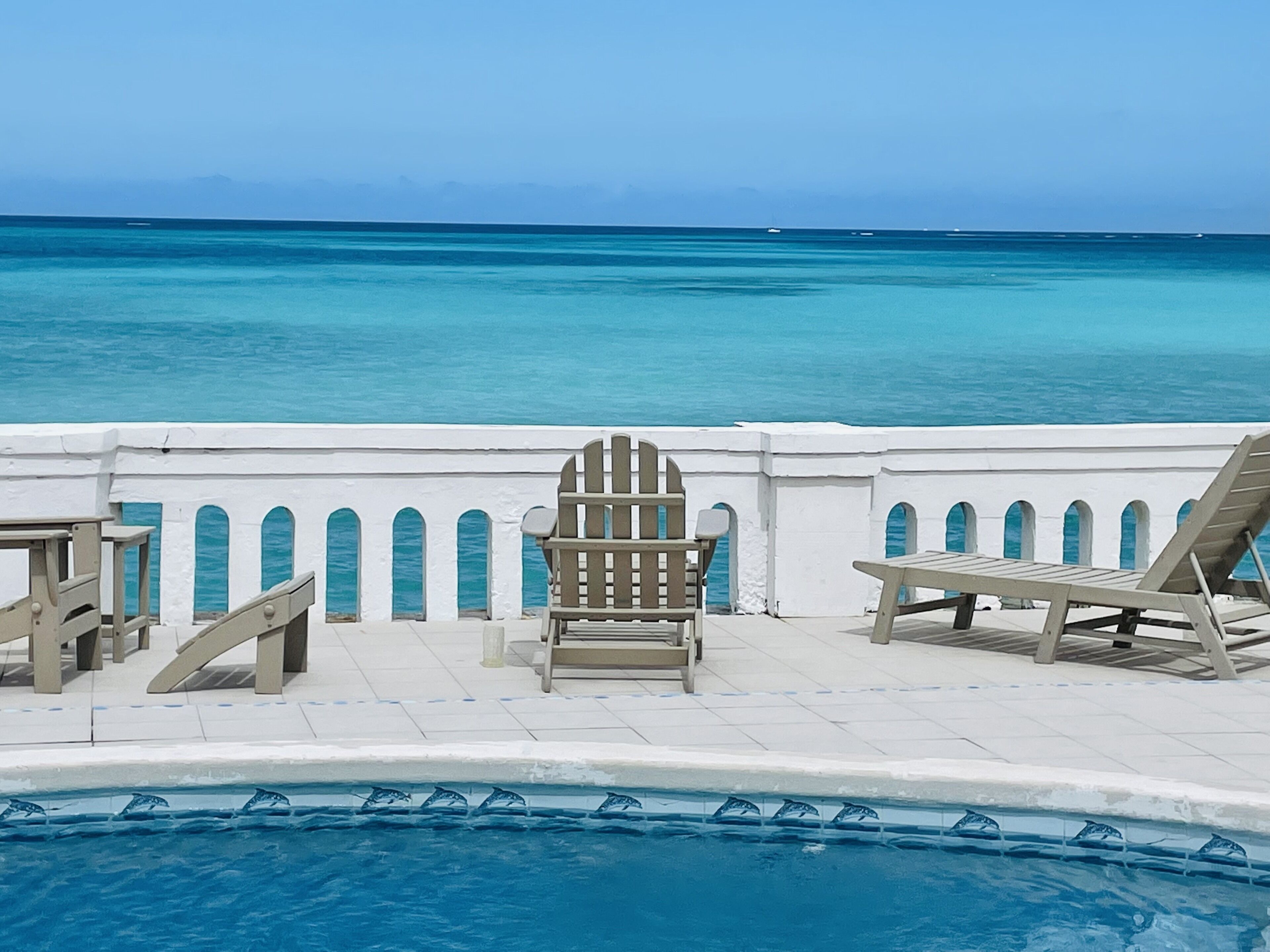 The pool deck with sun loungers, a white balustrade, and the sea.