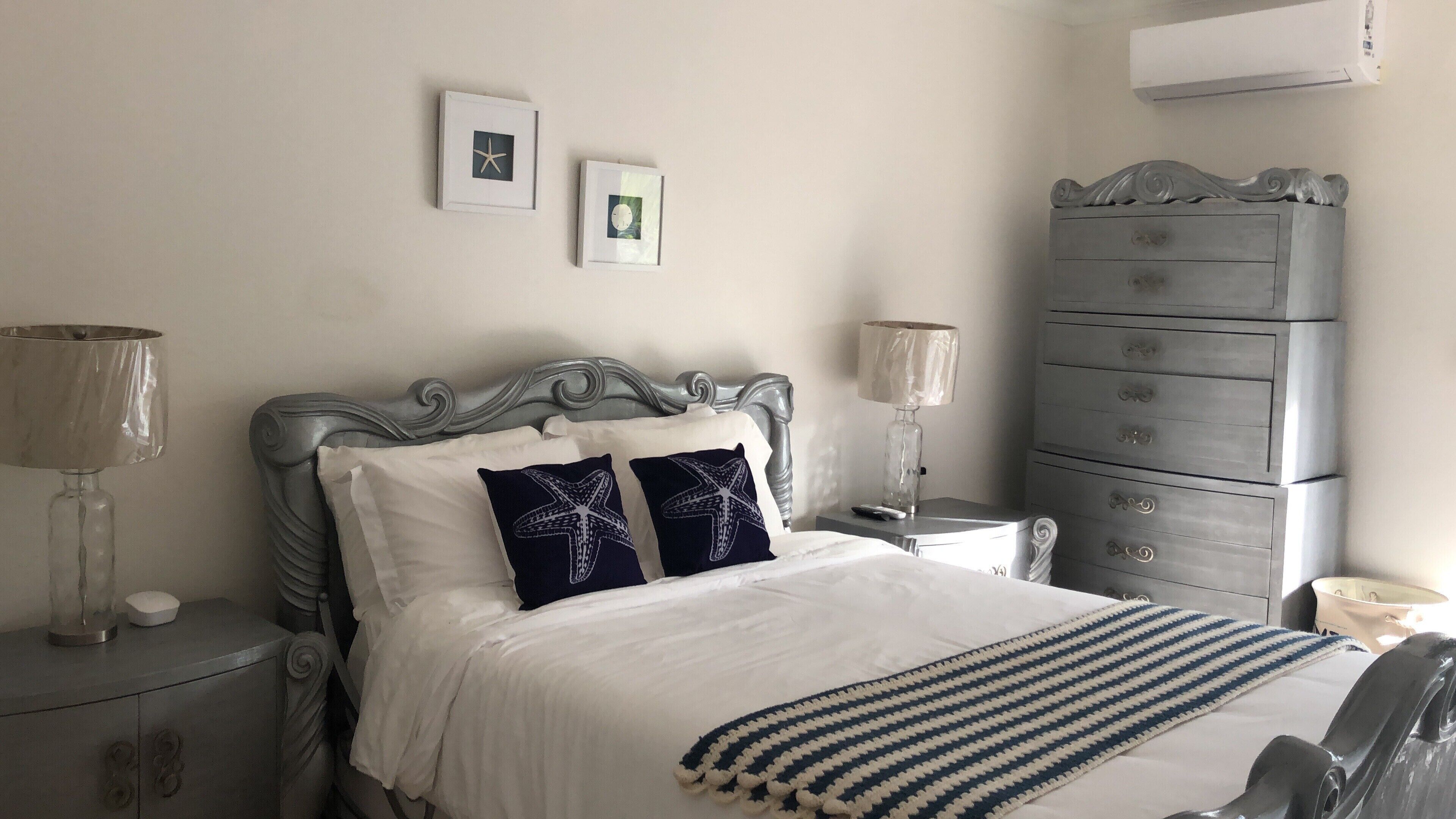 A bedroom with a silver bed, two lamps, and gray dressers.