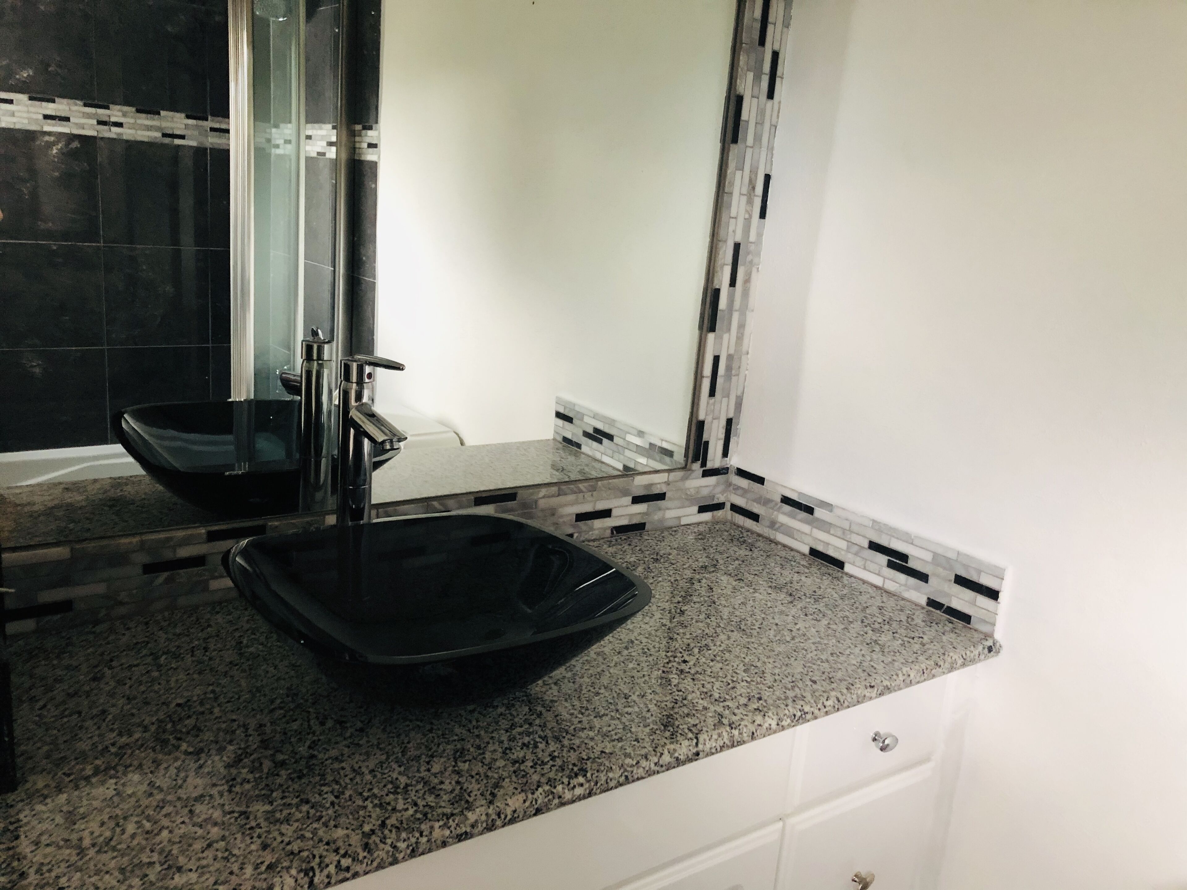 A bathroom with a black glass sink on a granite counter.