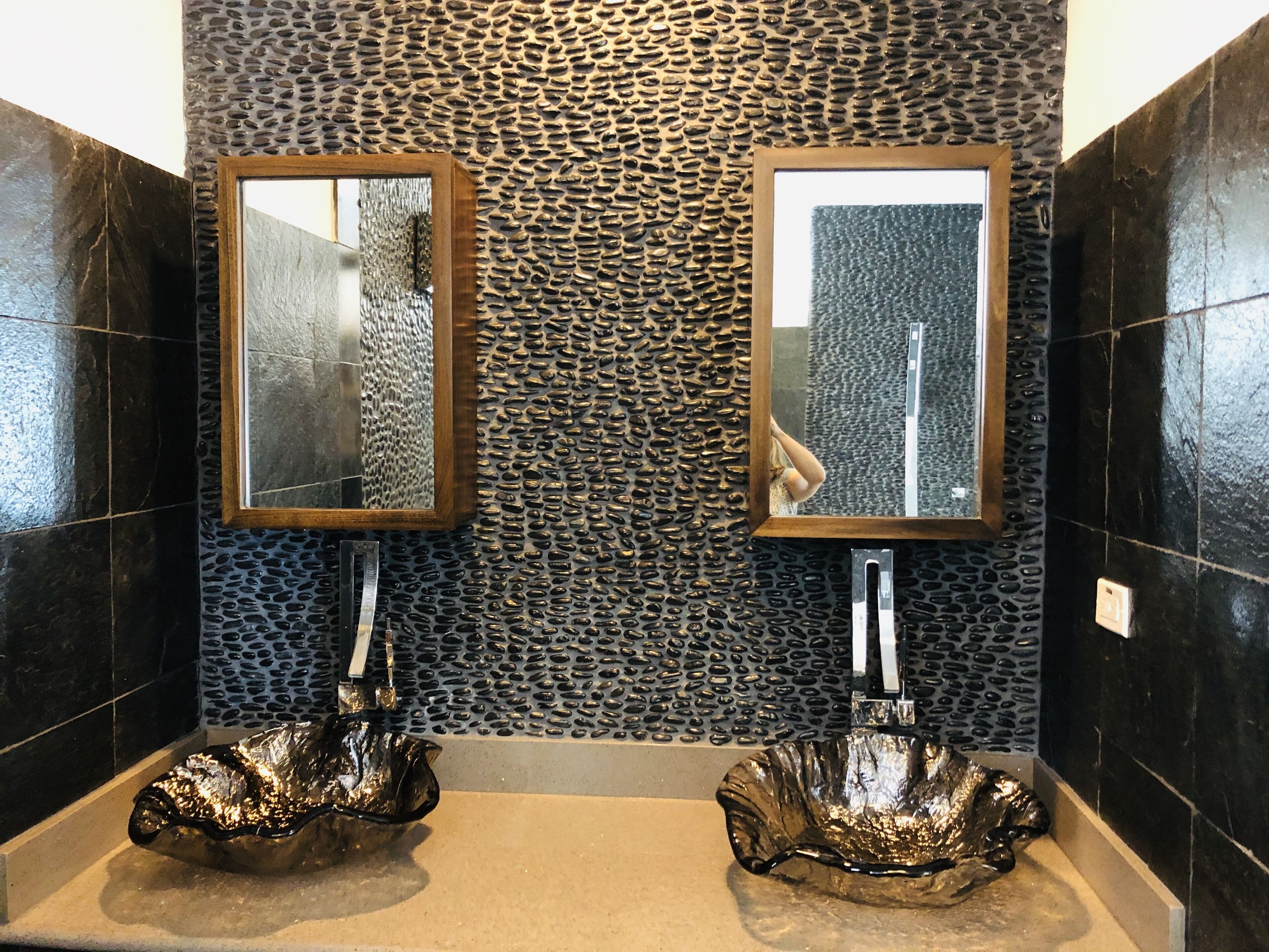 A bathroom with a pebble wall, two mirrors, and two glass sinks.