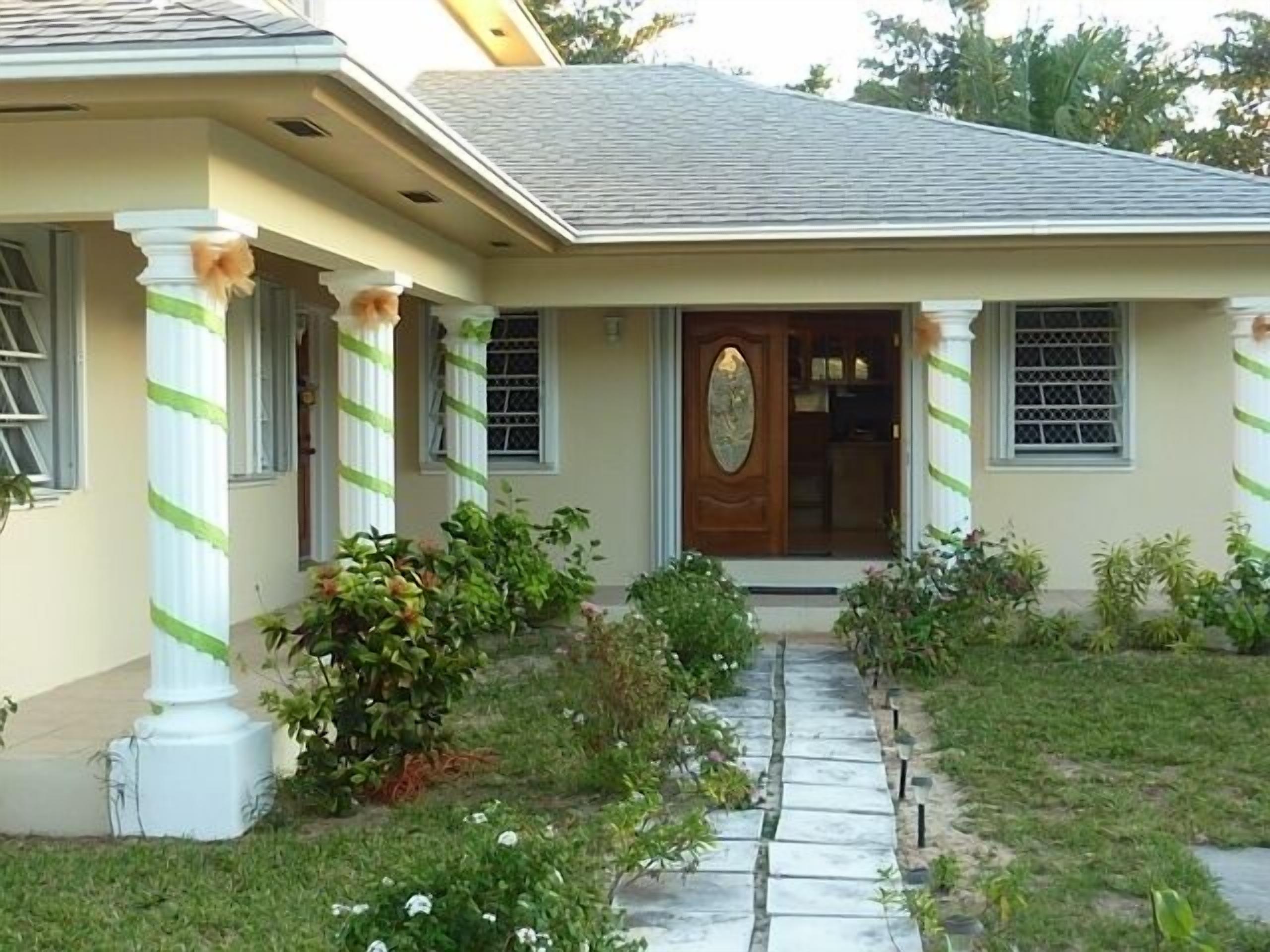The front entrance of the villa has a covered porch, white columns, and a garden path.