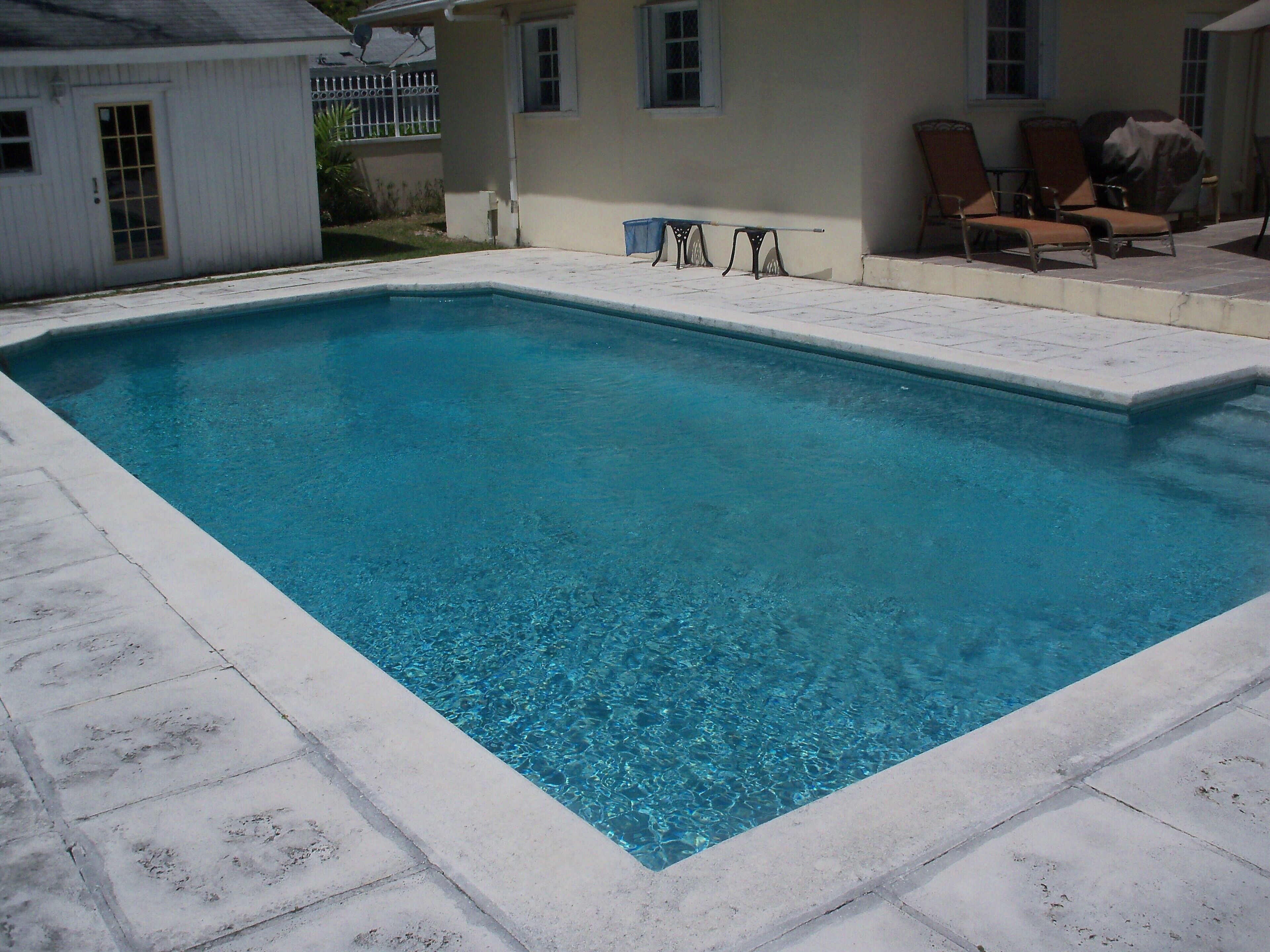 The pool has a ladder and a stone deck next to the villa.