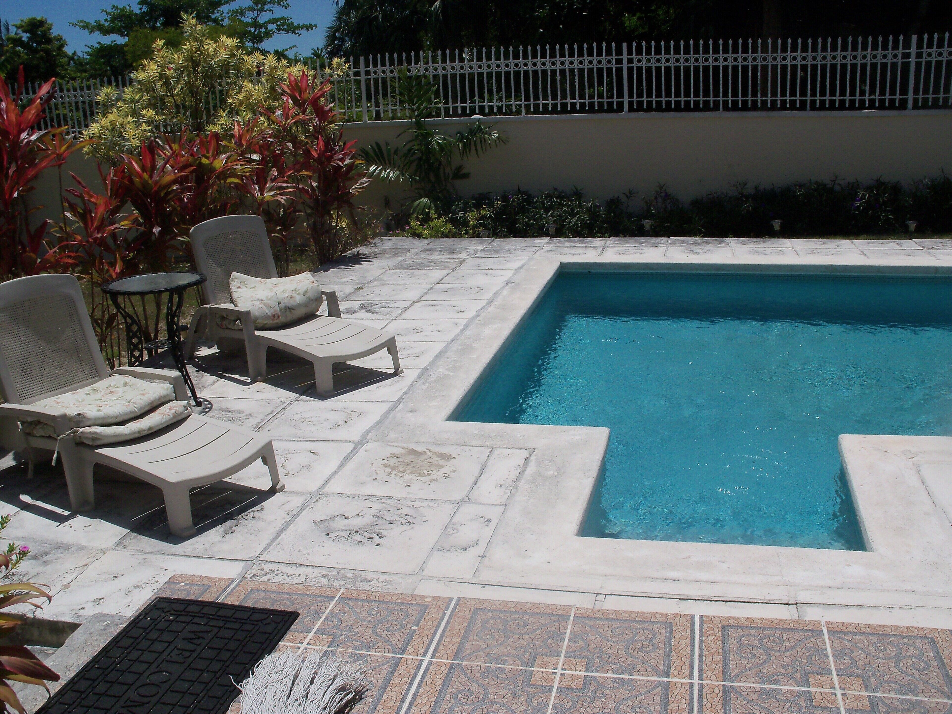 Two sun chairs and a small table stand next to the pool.