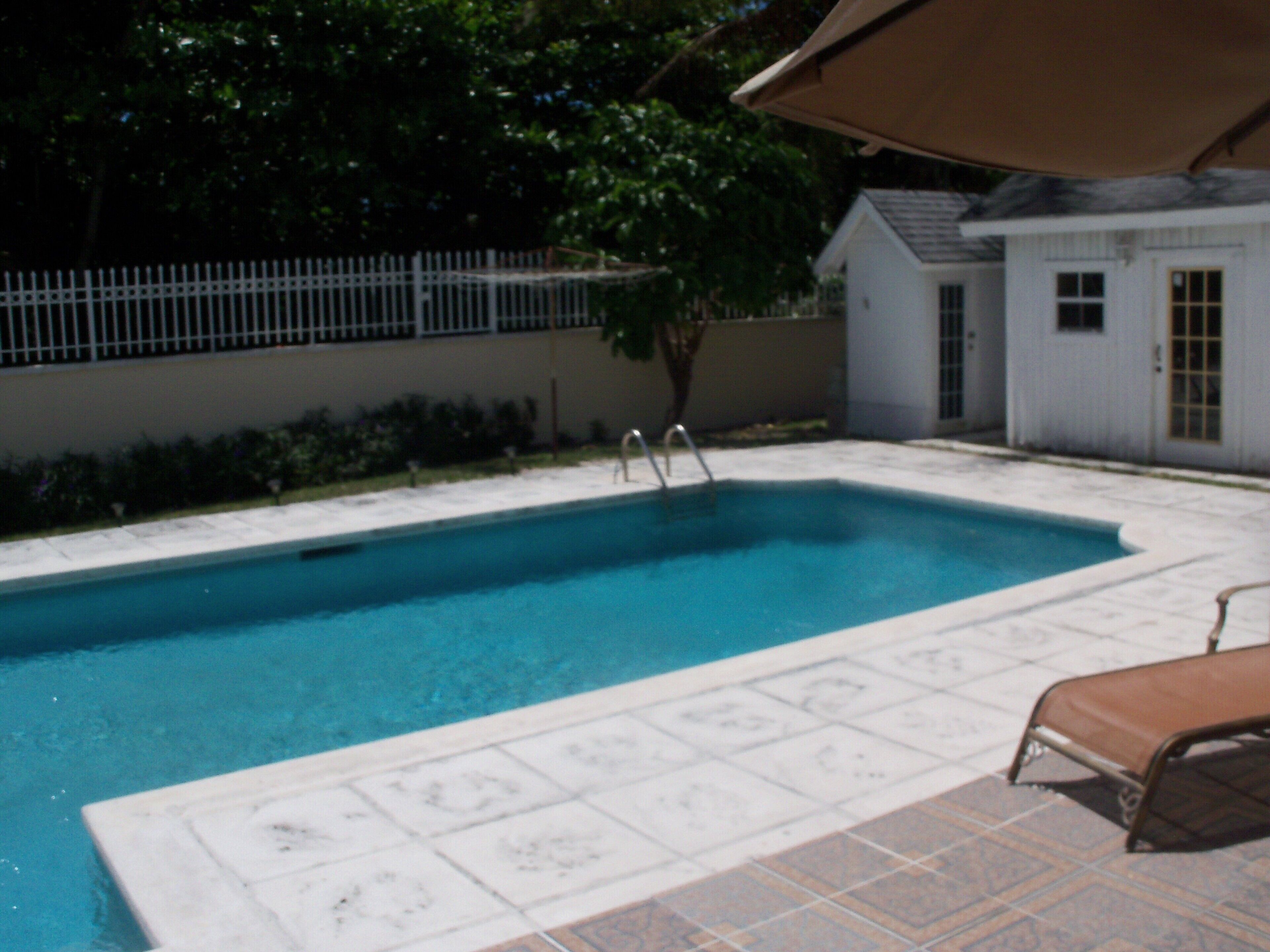 The pool has a white fence behind it and a pool house at the far end.