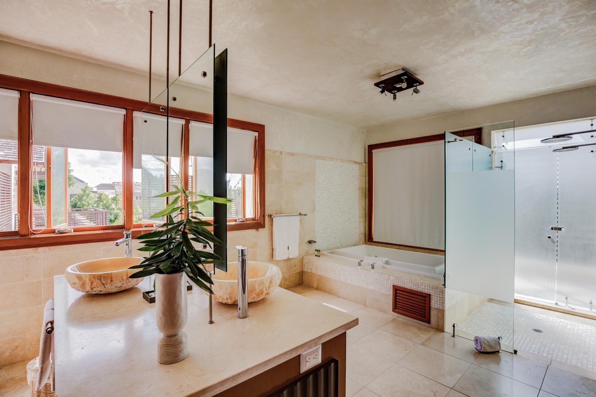 A bathroom with two stone sinks, a bath tub, and a glass shower.