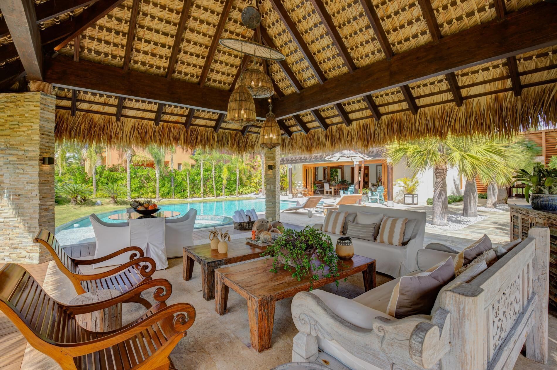 The inside of the gazebo with sofas, wood tables, and a view of the private pool.