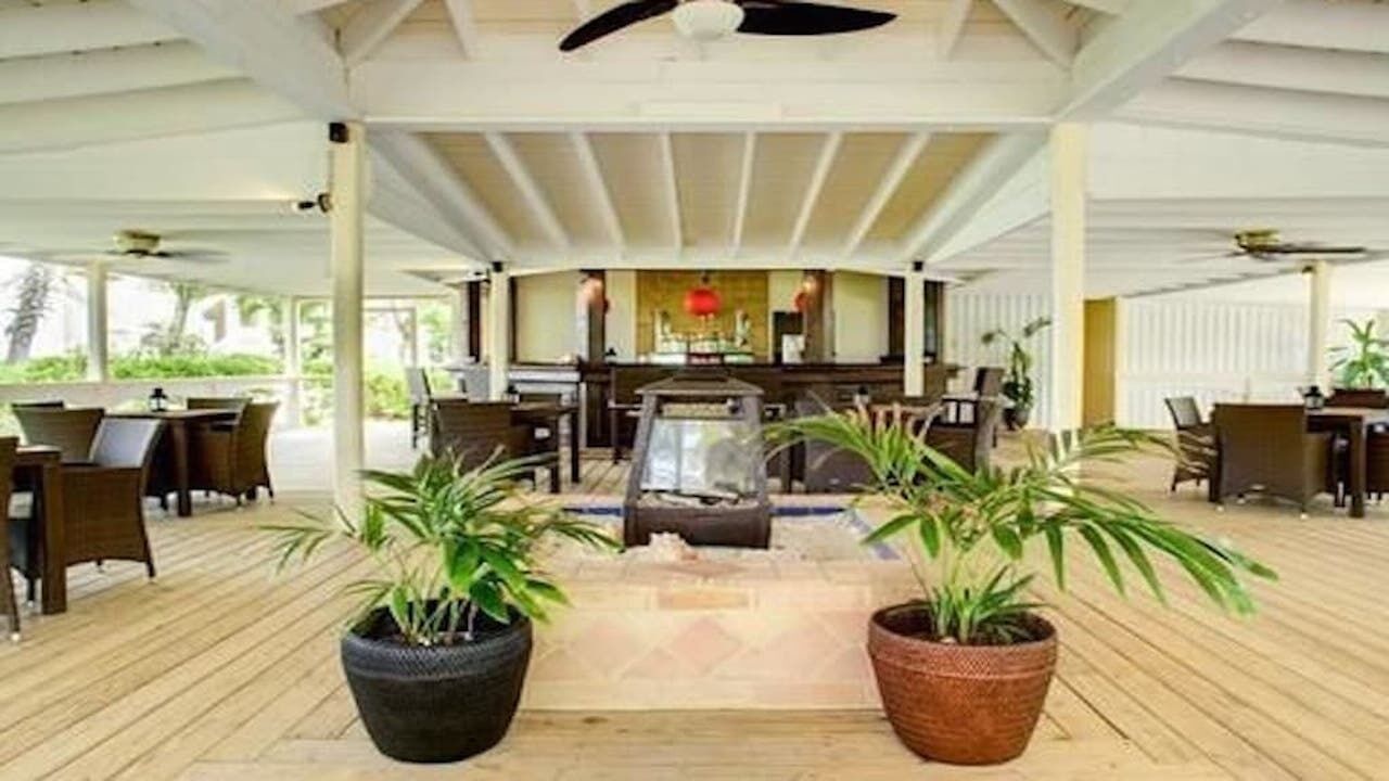 A covered lounge with plants, tables, and a bar.