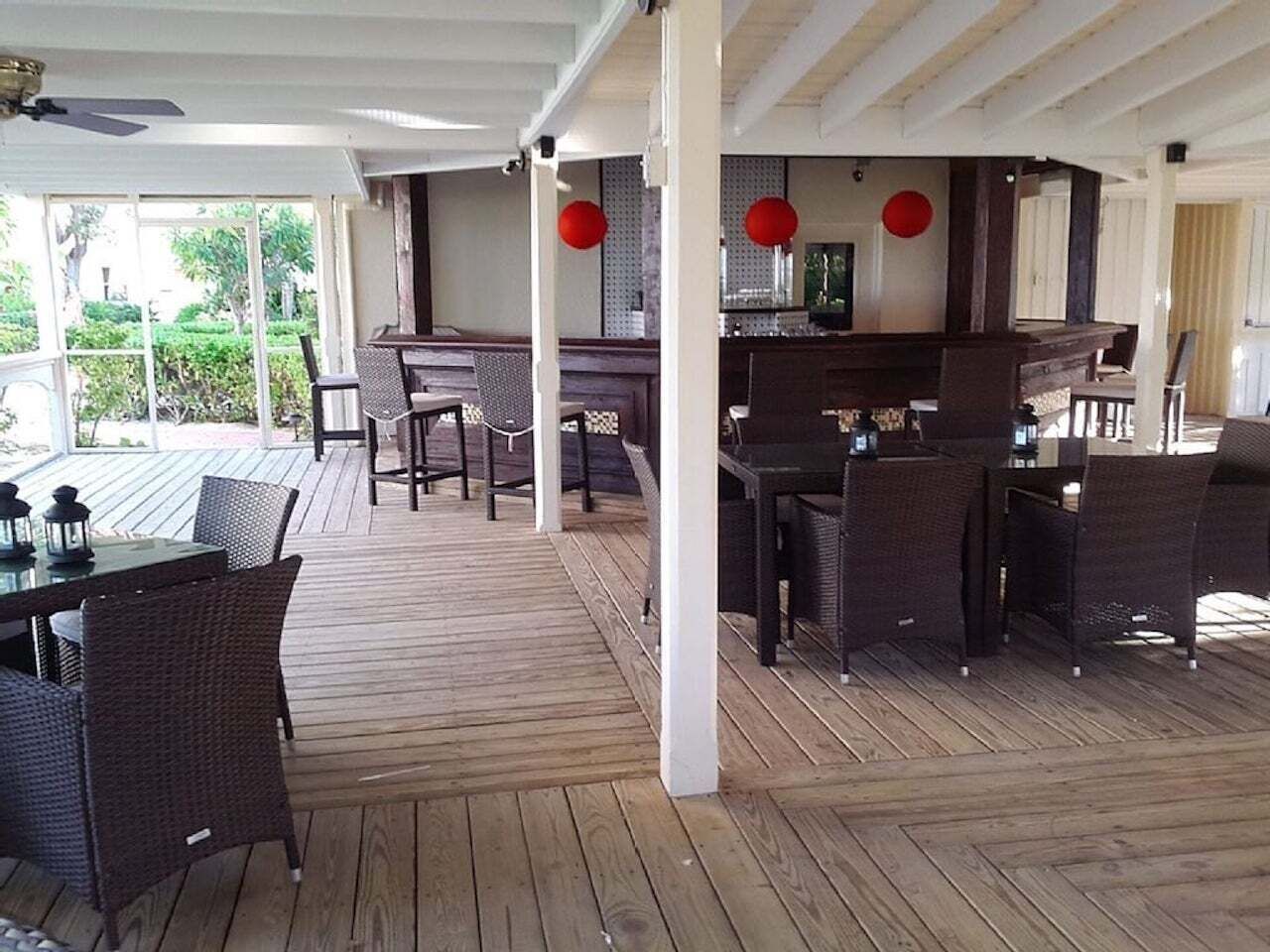 A covered deck with a bar, stools, and wicker chairs.