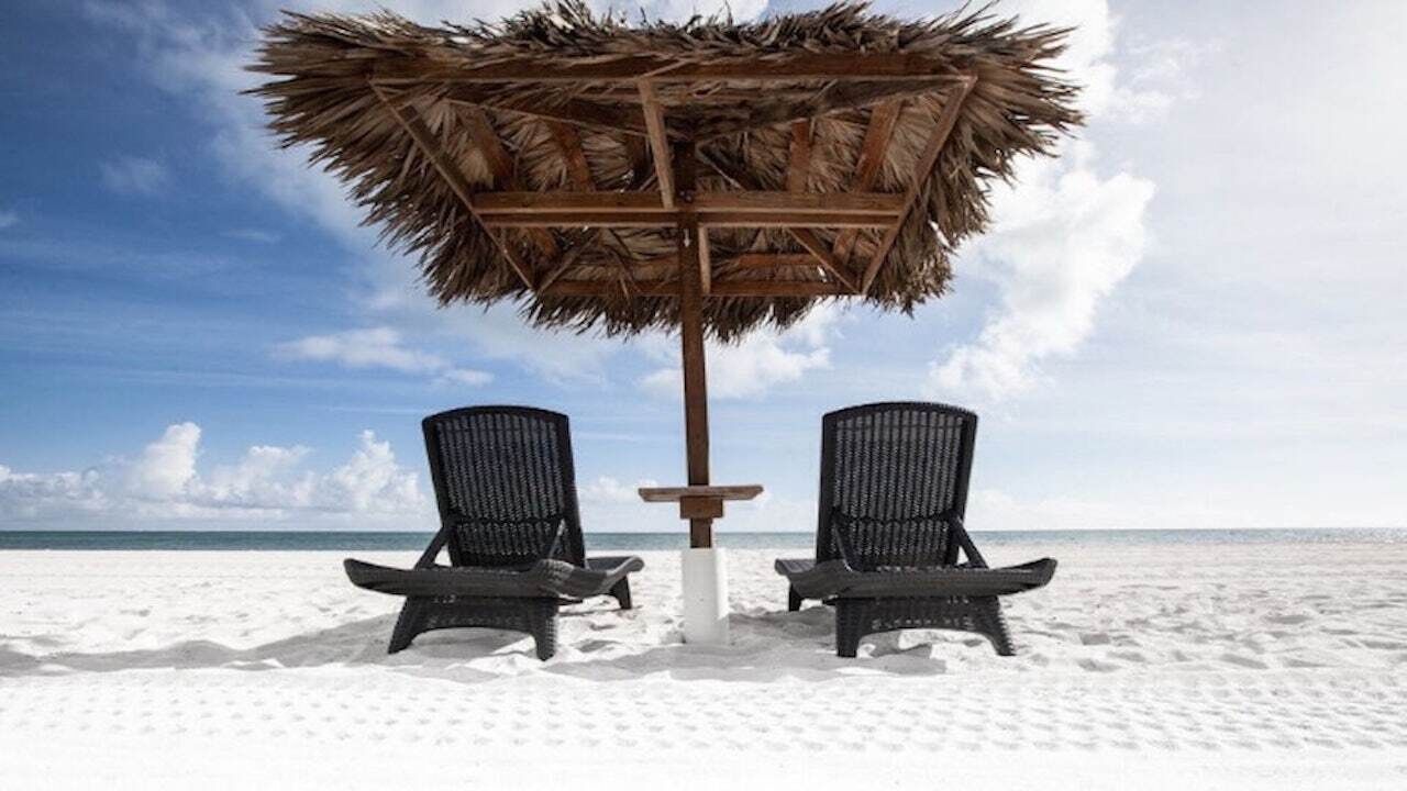 Two loungers under a thatch umbrella on white sand.