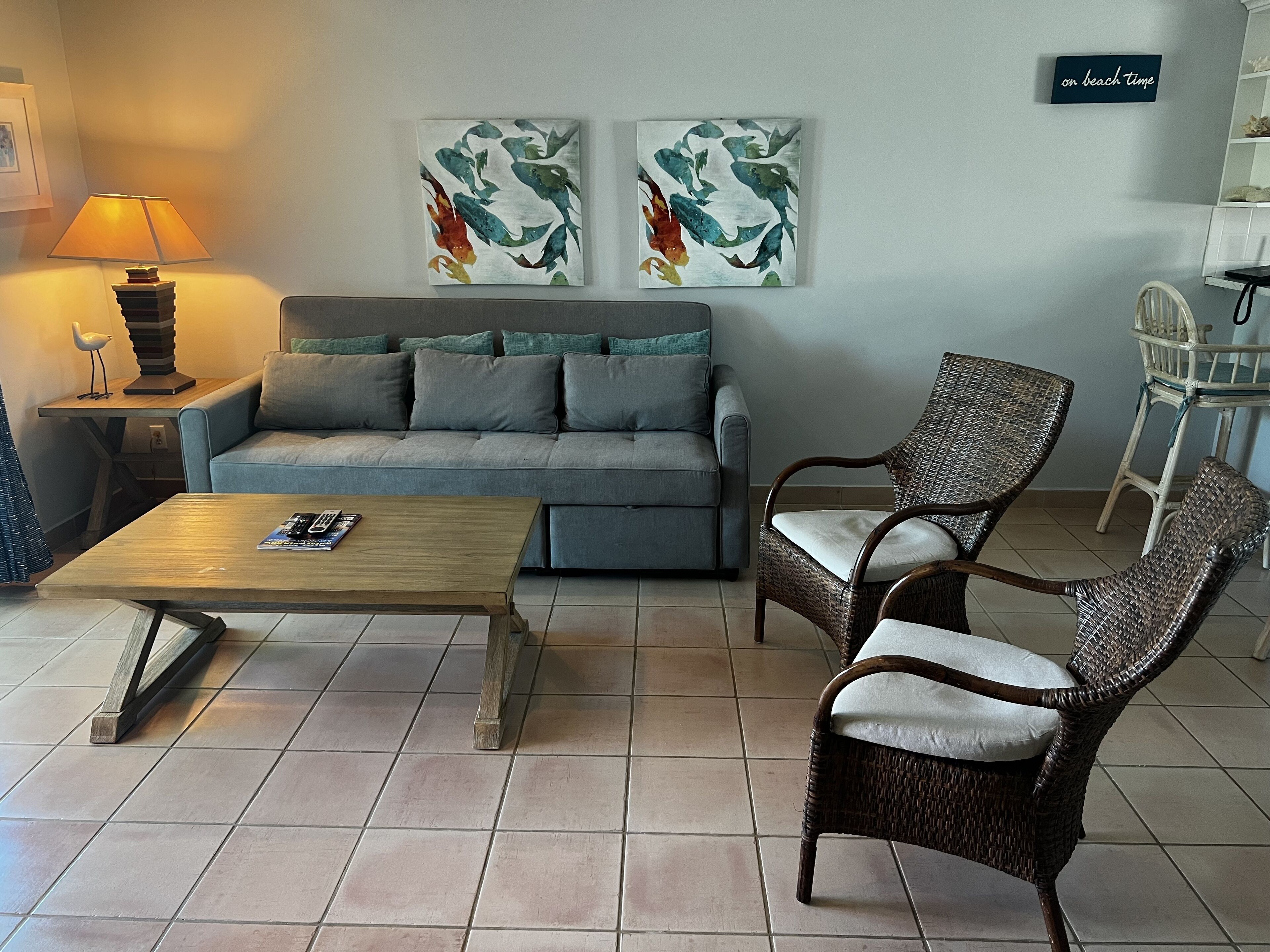 A living room with a gray sofa and two fish paintings.