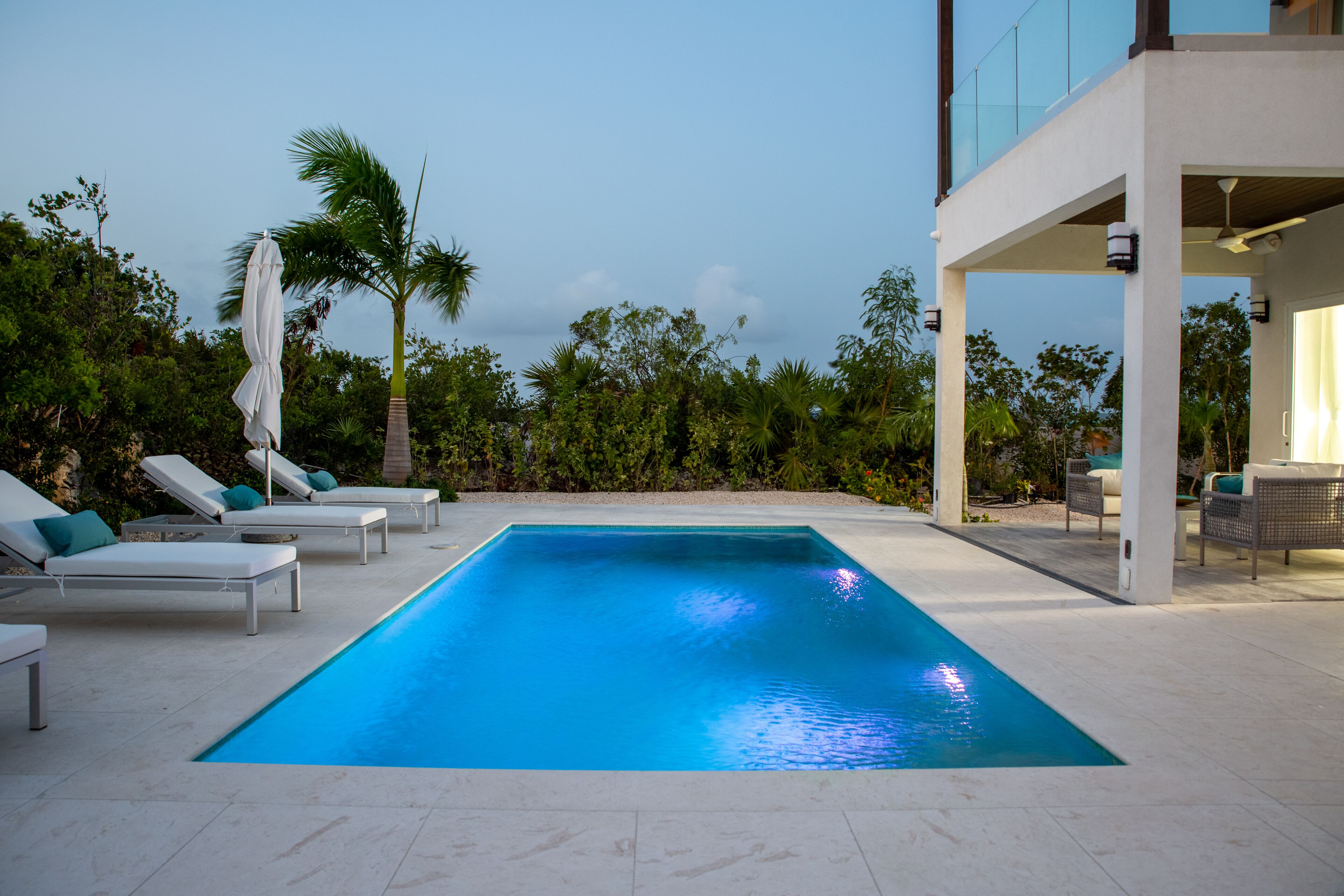 The pool with lights, loungers, and the covered terrace at dusk.
