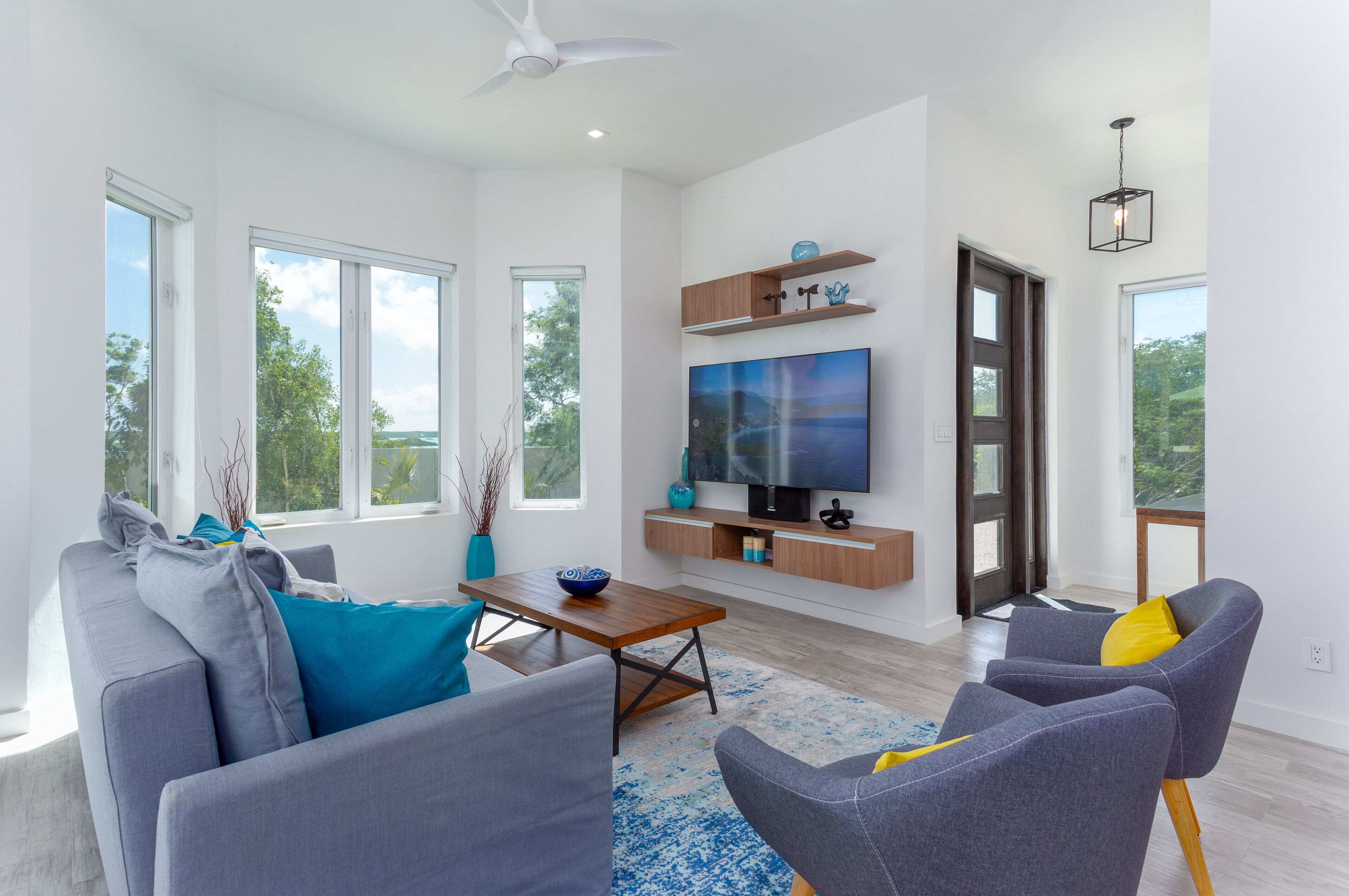 A living room with a gray sofa, blue pillows, and a television on the wall.