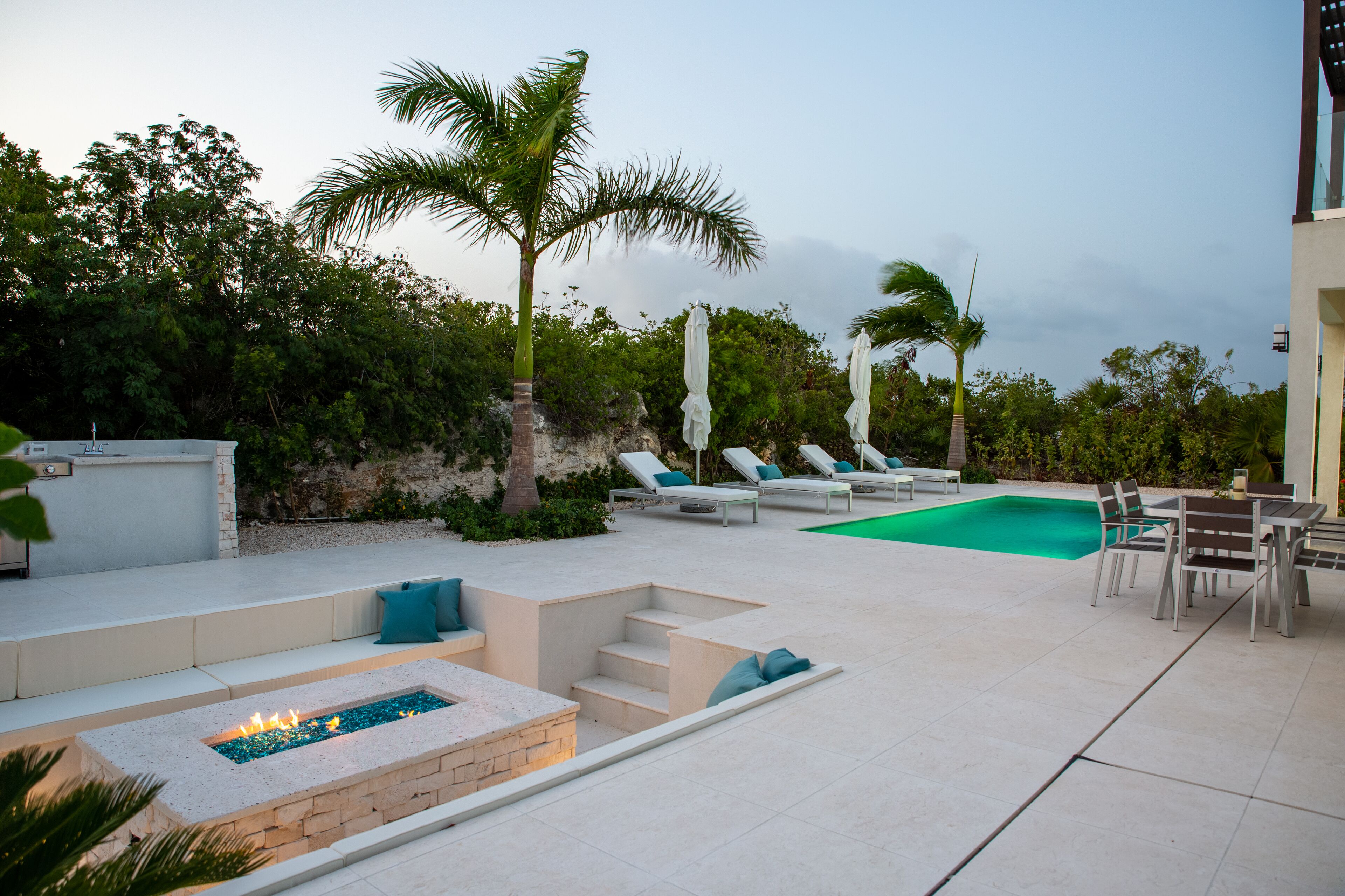 A sunken lounge with a fire pit next to the pool at dusk.