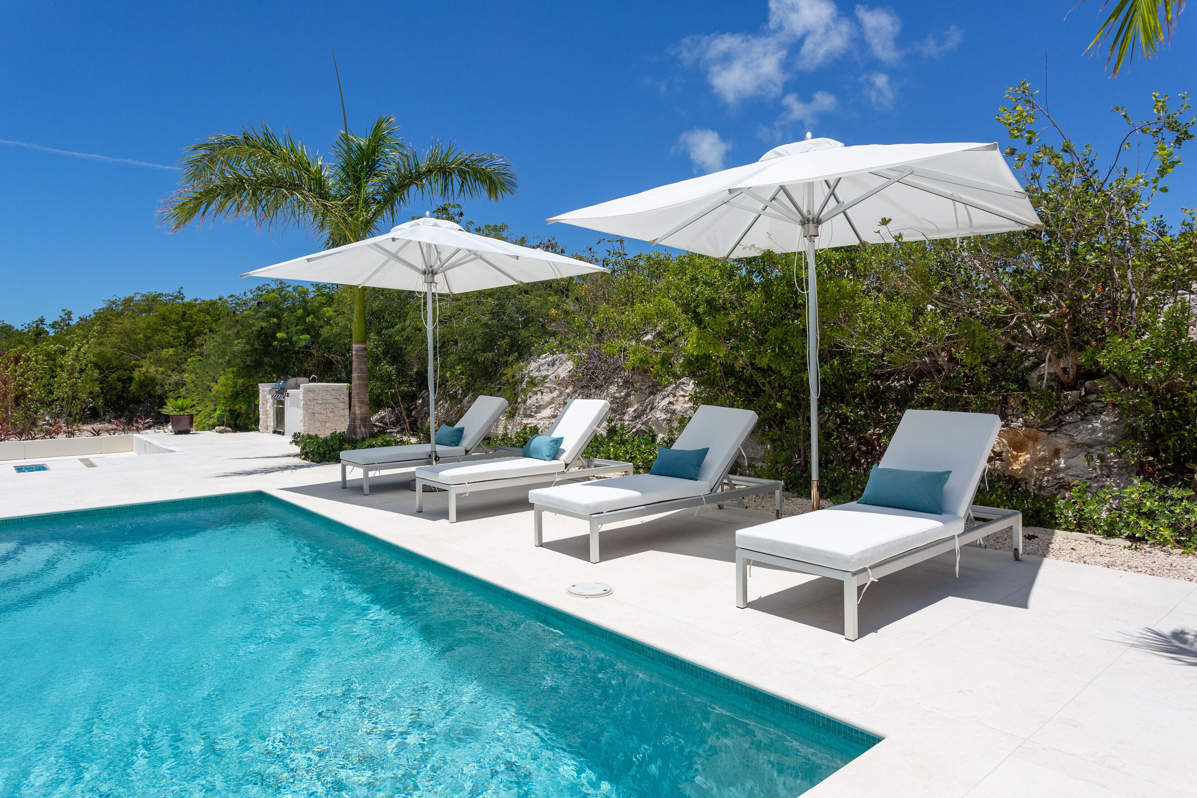The pool with four loungers and two white umbrellas.
