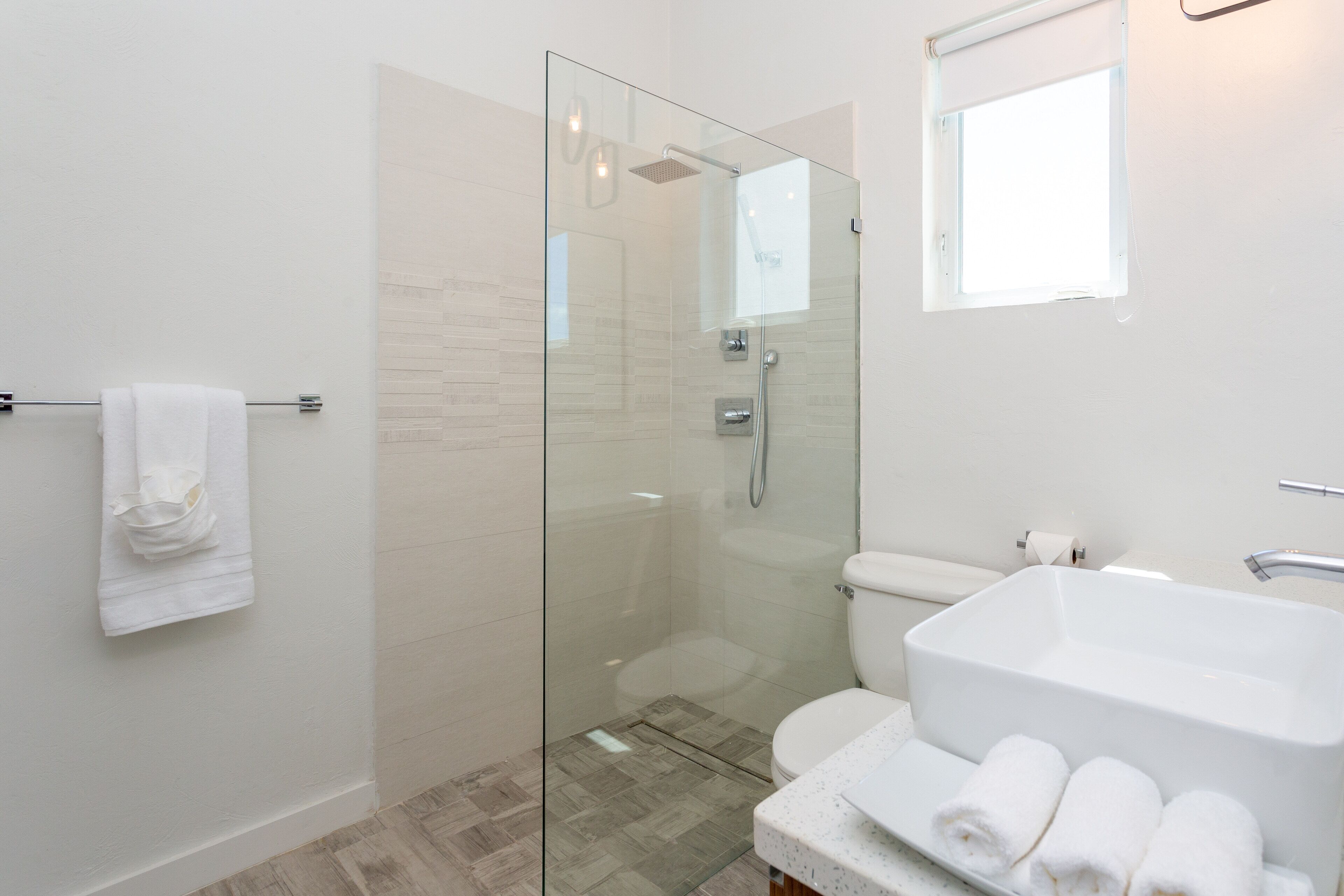 A bathroom with a glass shower, a toilet, and a white bowl sink.