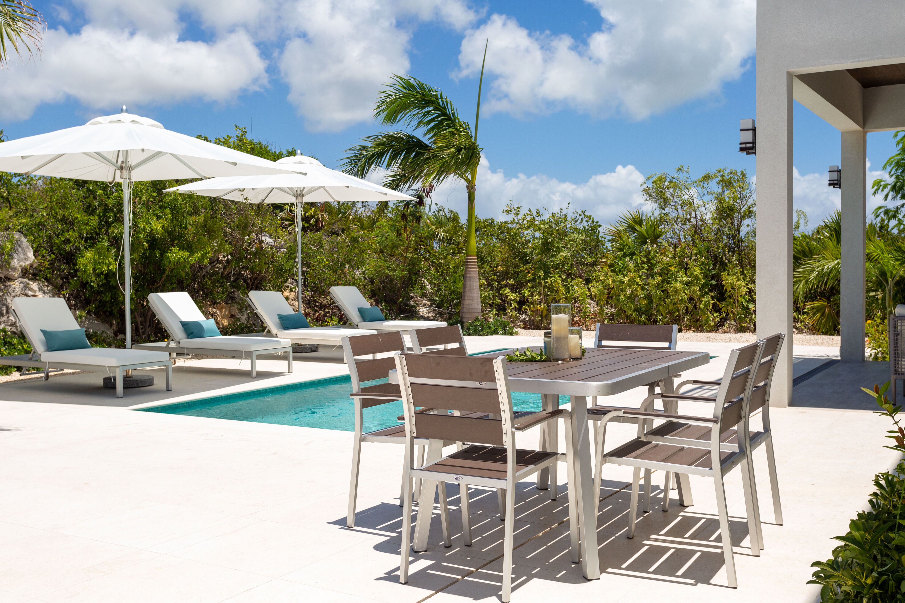 An outdoor dining table next to the pool, with umbrellas and loungers.